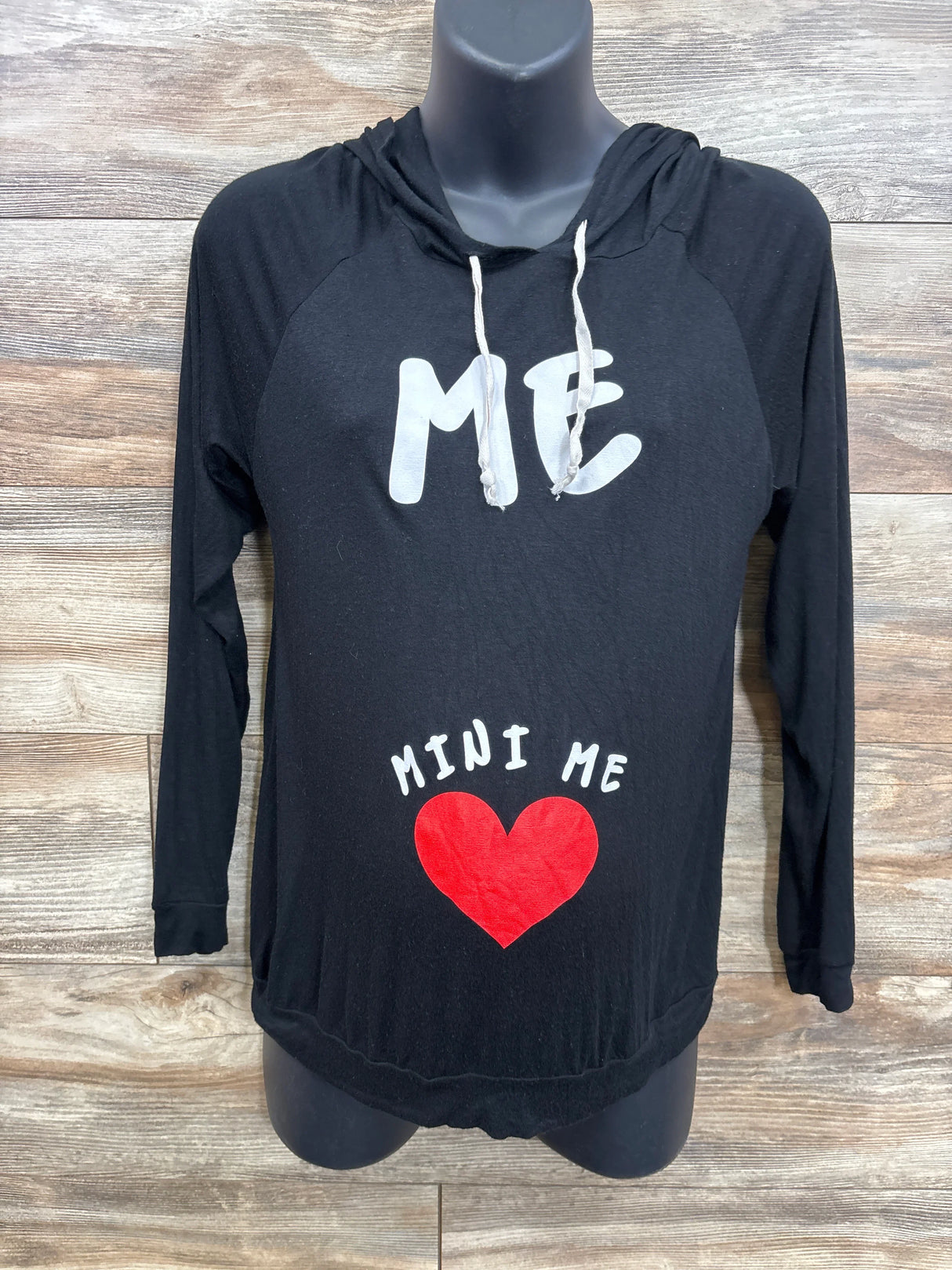 Black maternity hoodie with 'ME' text, 'MINI ME' and red heart on belly, wooden background