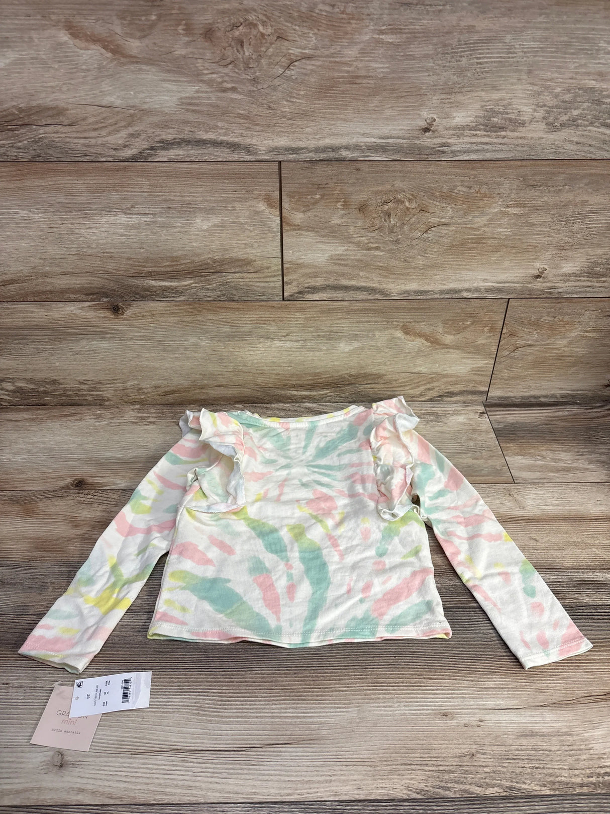 Toddler long sleeve ruffle shoulder top in pastel tie-dye colors on wood background