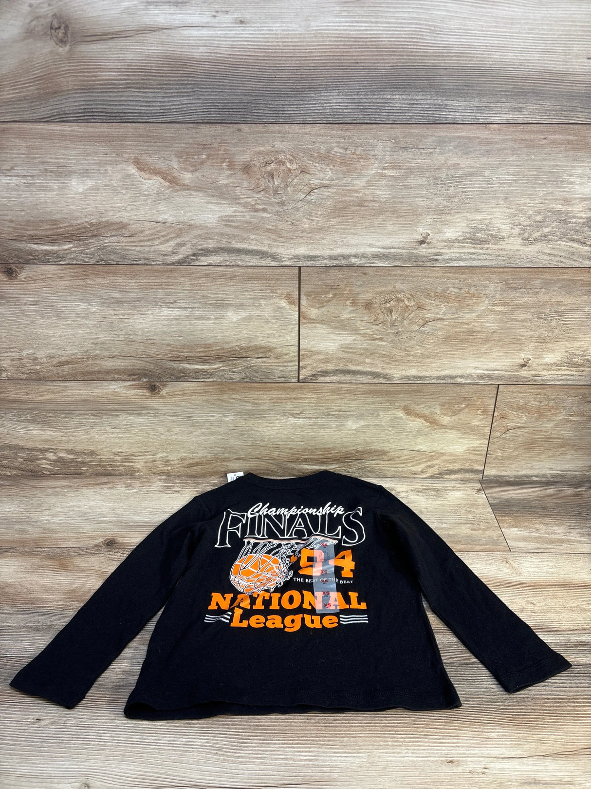 Black kids long sleeve shirt with 'Championship Finals 94 National League' graphic on wood floor