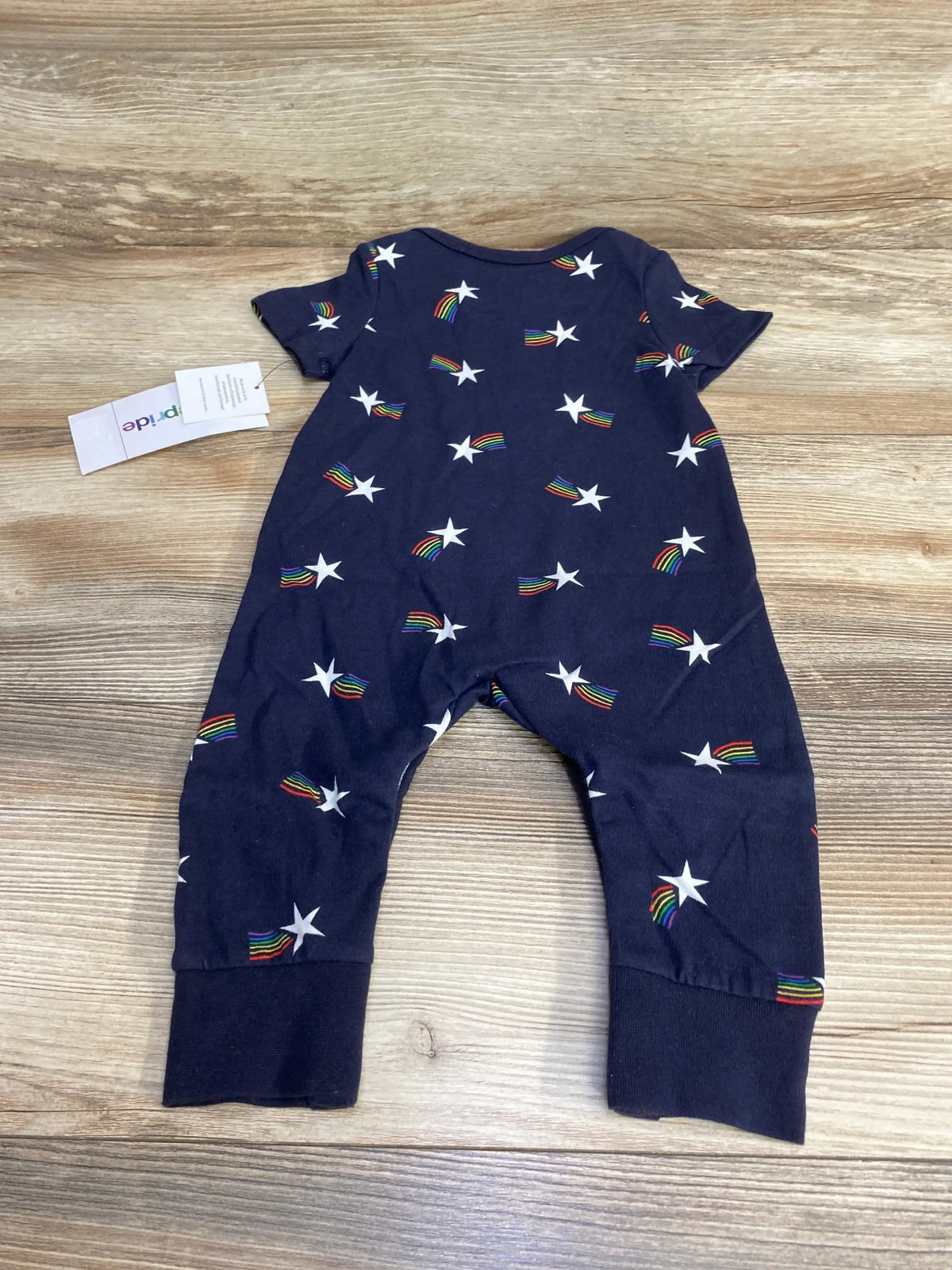 Flat-lay of navy baby romper size 3-6 months with white stars and rainbow shooting-star print, short sleeves and cuffed ankles on wood