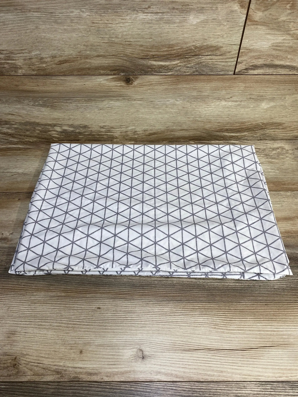 Top-down view of Graco Travel Lite crib sheet folded, white fabric with grey geometric triangle pattern on wood background