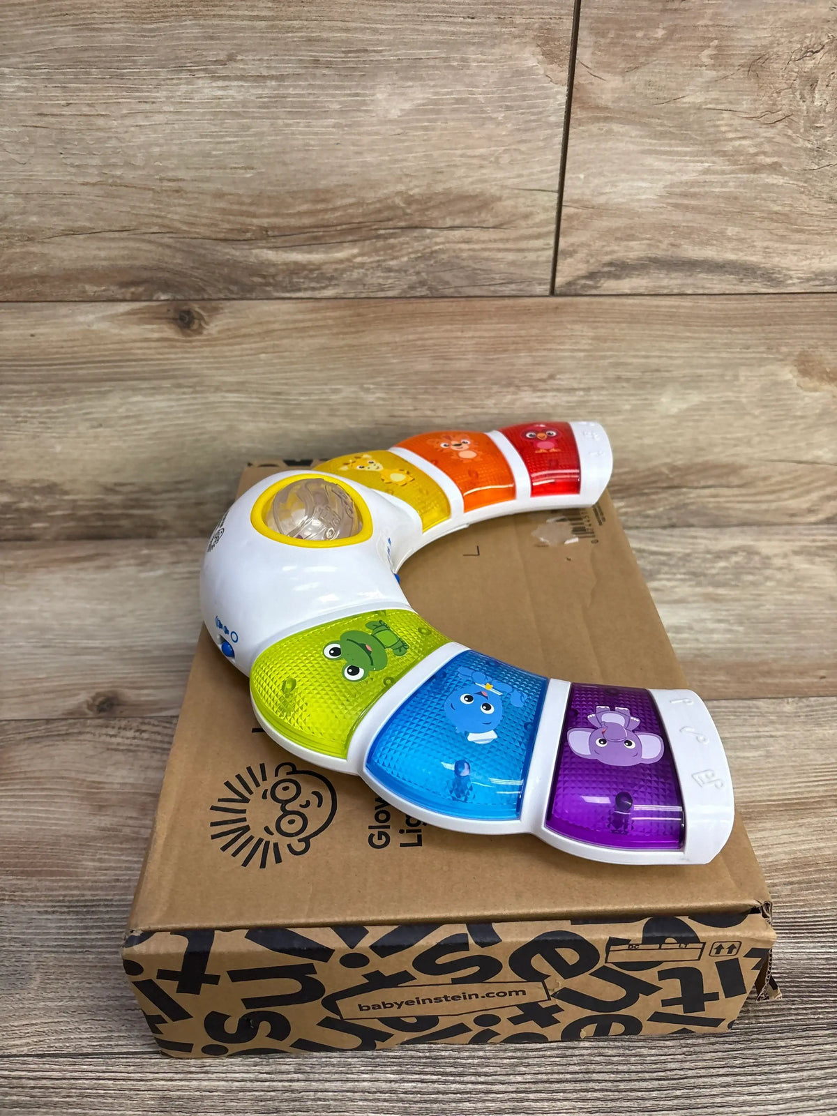 Angled view of Baby Einstein Glow & Discover Light Bar showing rainbow light panels with animal illustrations on a cardboard box