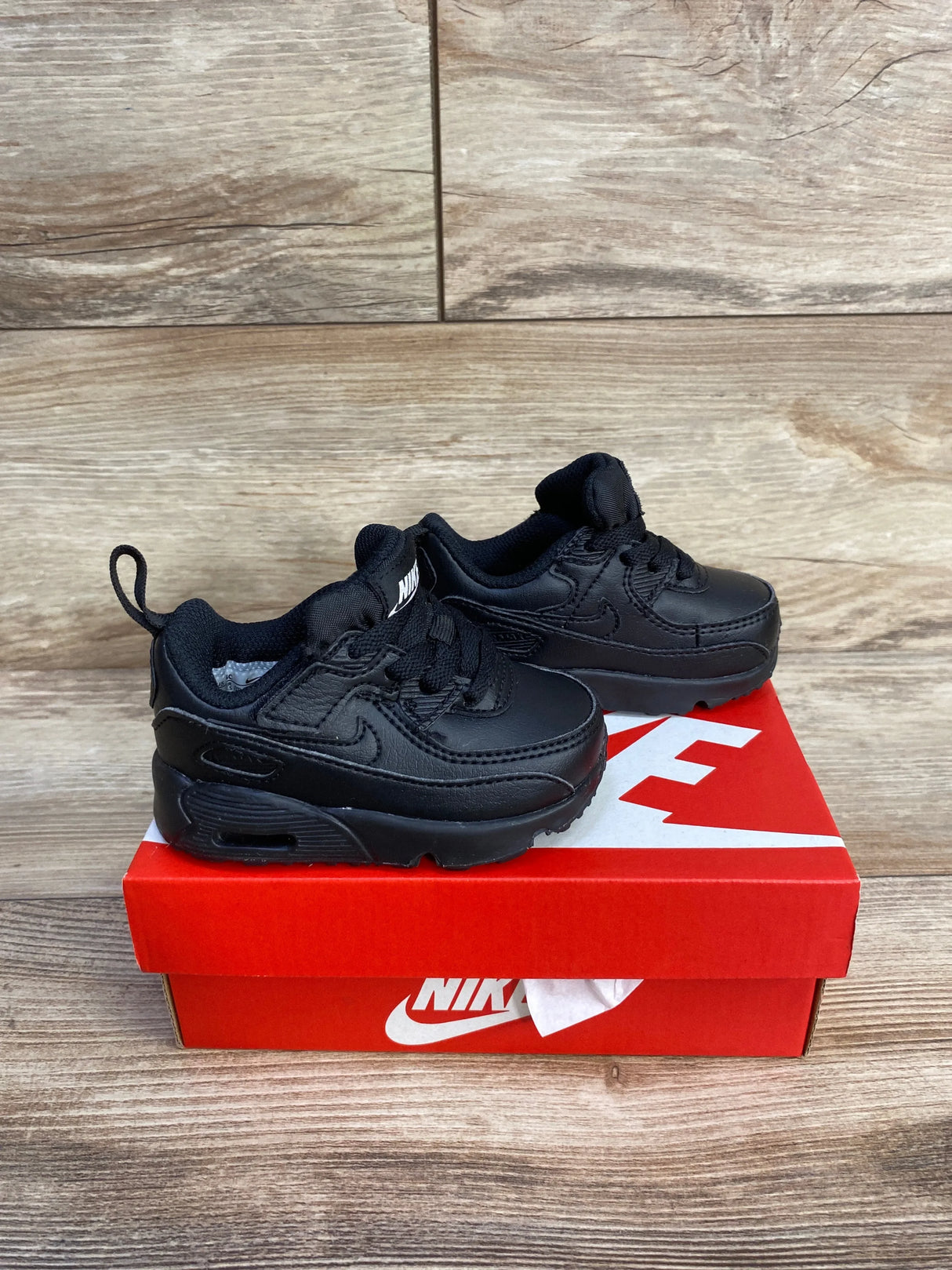 Three-quarter view of Nike Air Max 90 EasyOn TD sneakers in triple black with Air unit and heel pull tabs on a red box