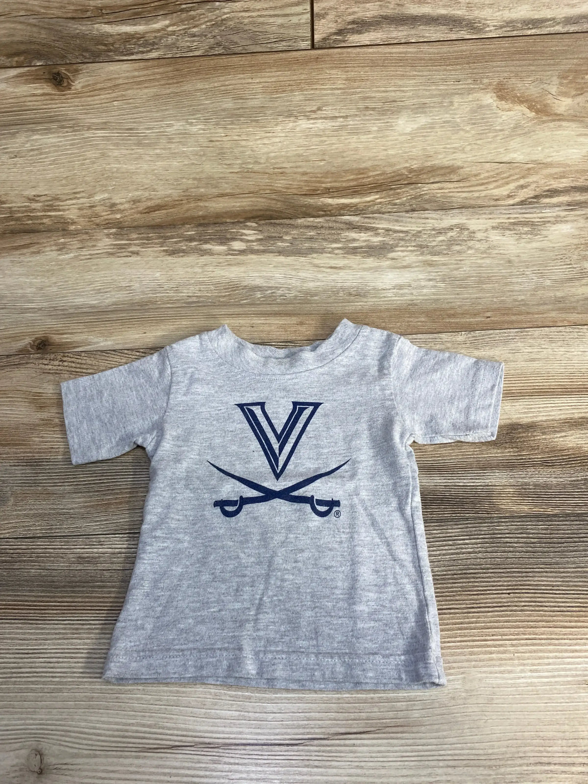 Gray toddler t-shirt with blue V logo and crossed sabres, on wooden floor background