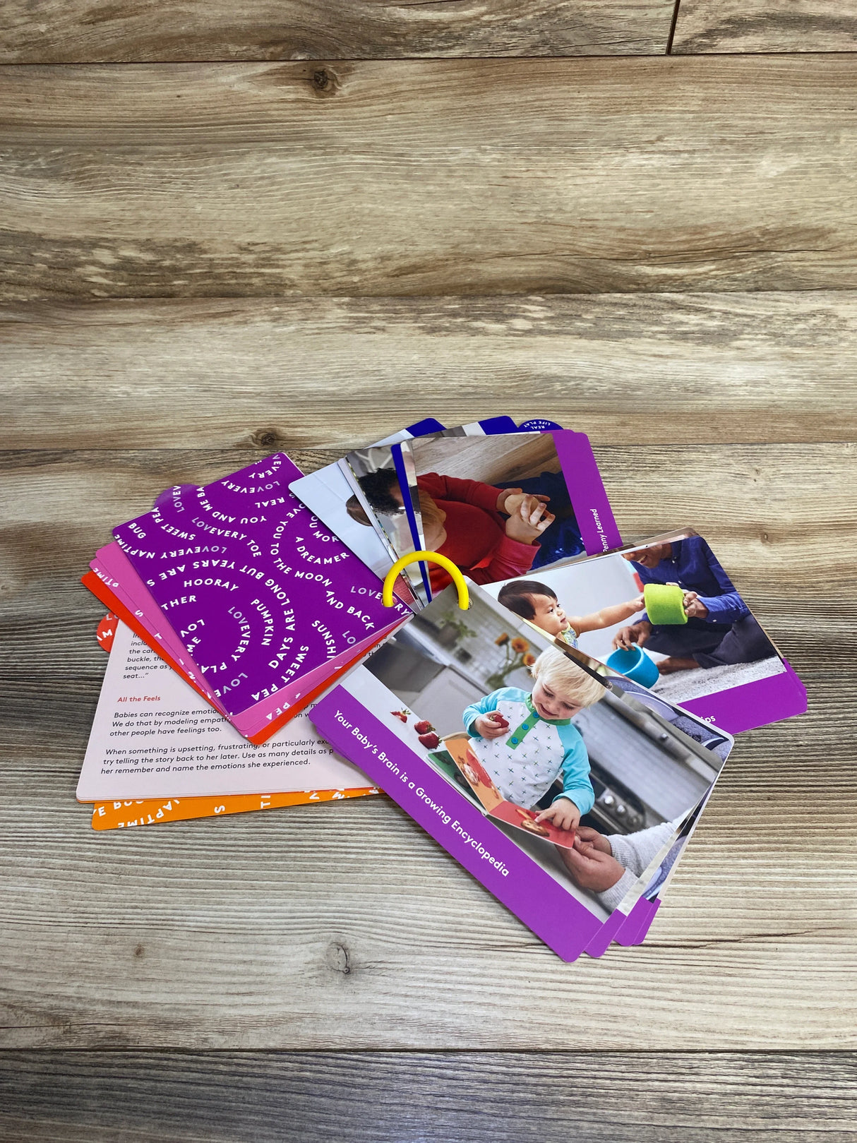 Baby development flashcards fanned out on wood surface with colorful photos and text