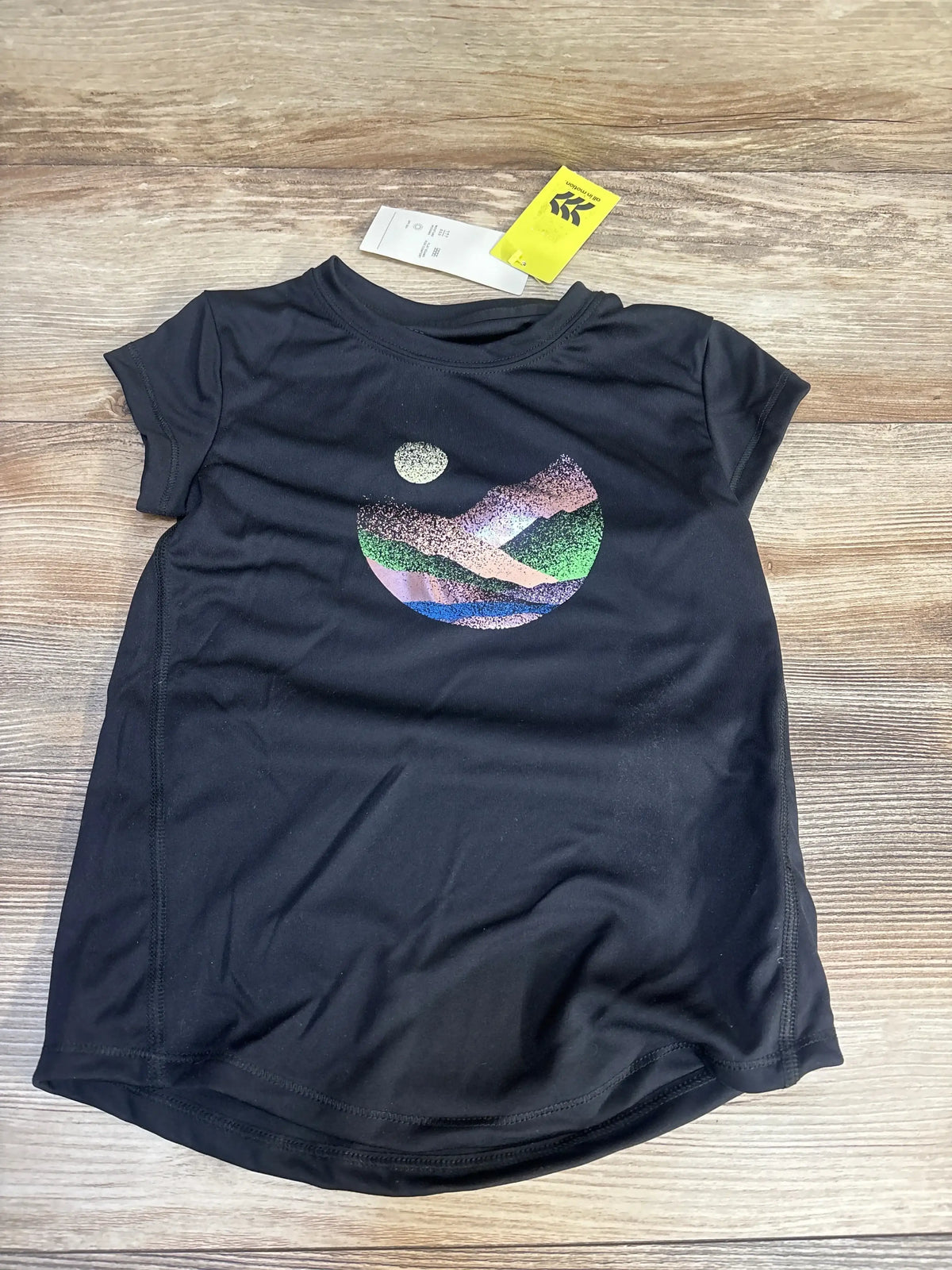 Flat-lay of 4T black short-sleeve active shirt with sparkly mountain-and-moon graphic on wood background, tags attached