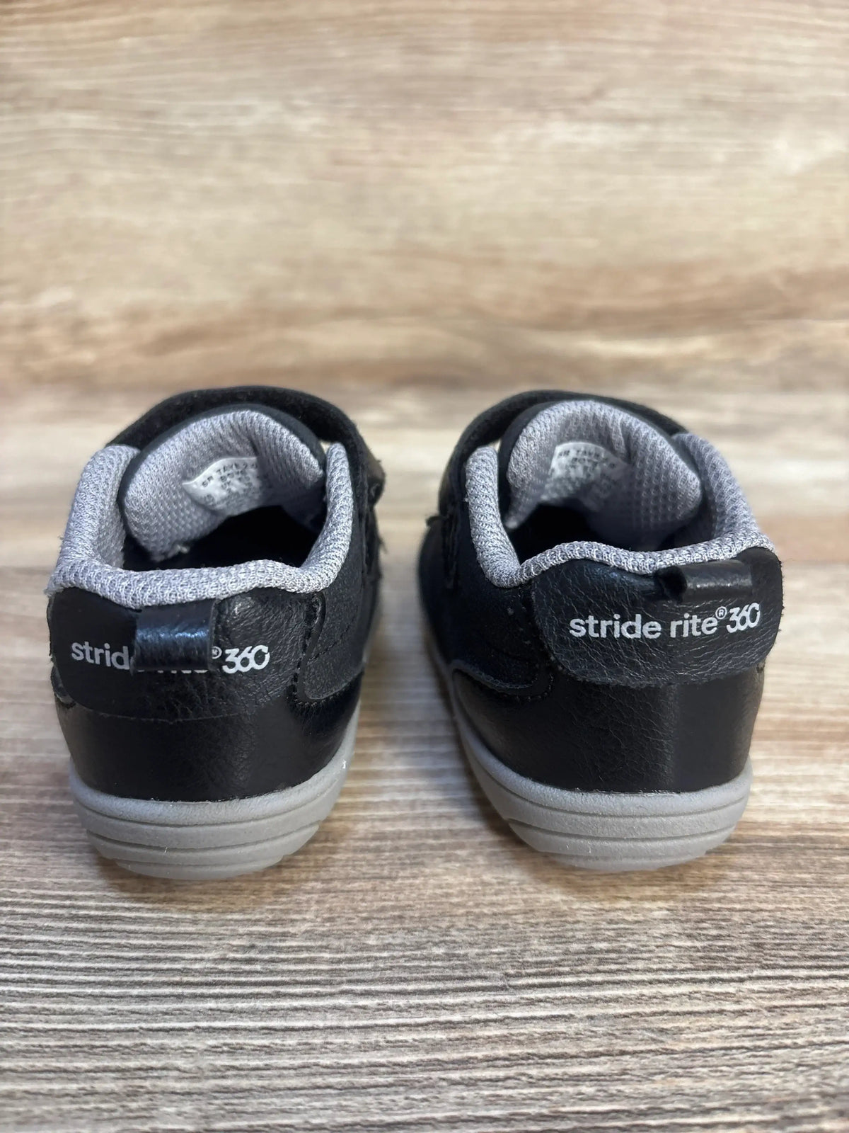 Black Stride Rite 360 toddler shoes with gray lining on wooden surface, rear view