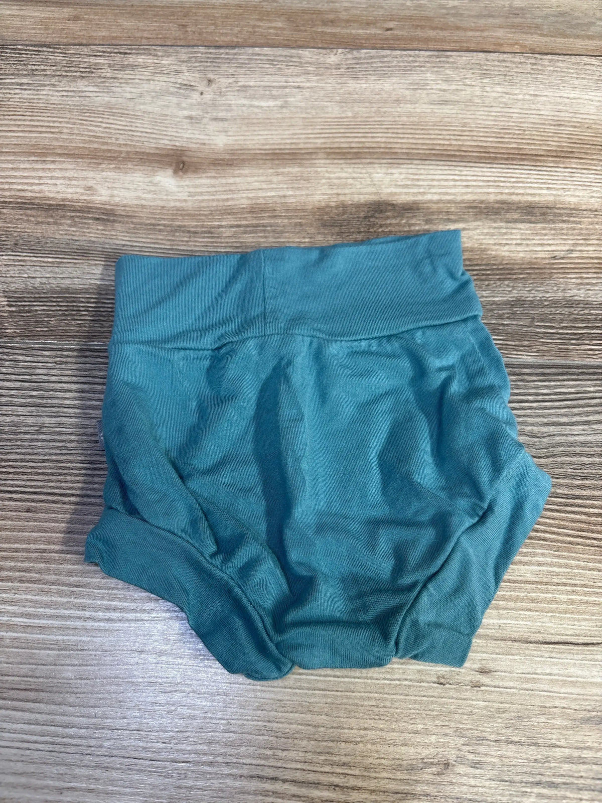 Top-down view of Kyte Baby bamboo bummies size 0-3M in teal showing wide foldover waistband and gathered leg openings on wood background