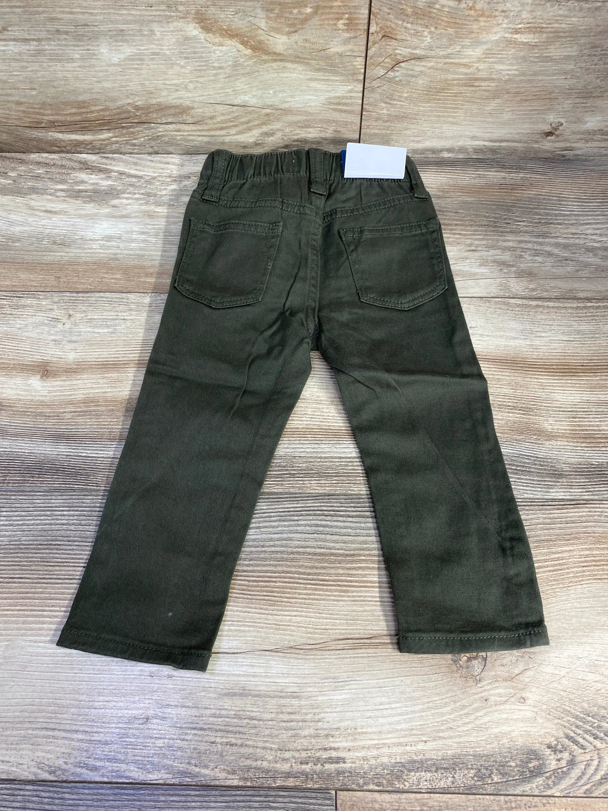 Olive green toddler pants with elastic waistband and back pockets on wood floor
