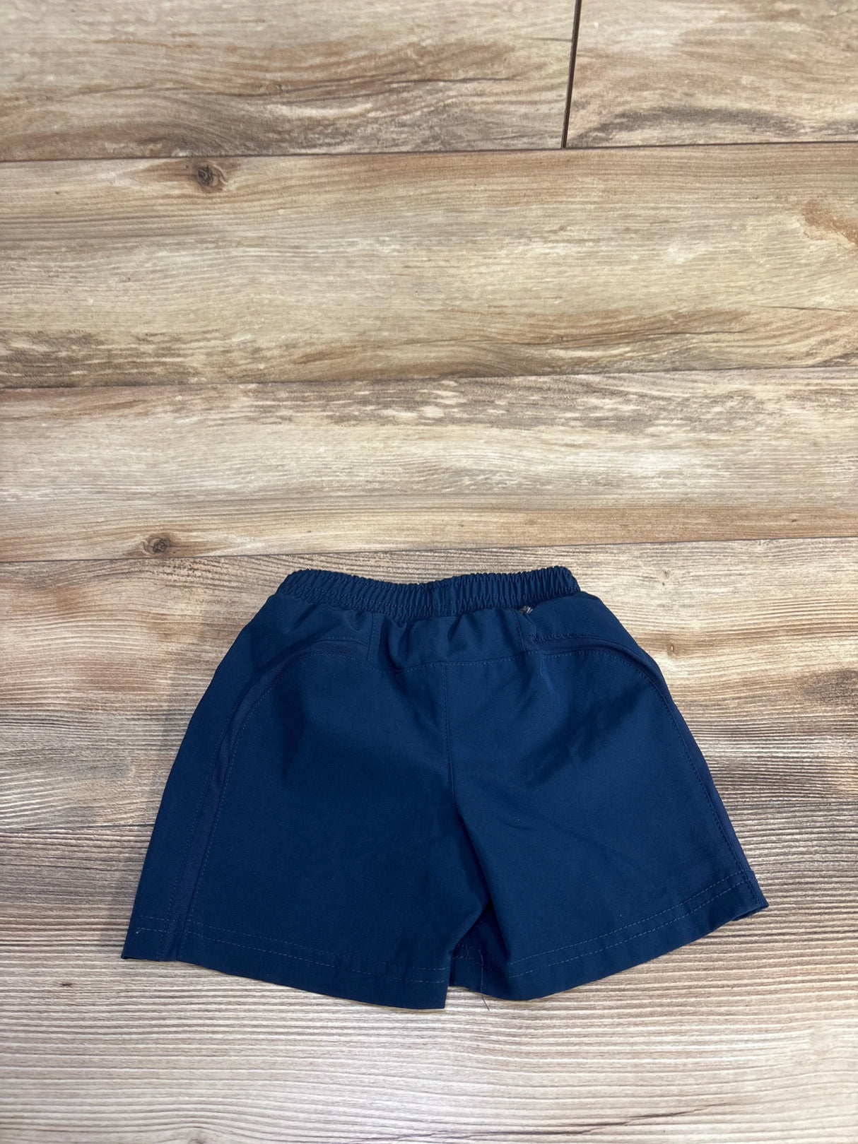 Flat lay of navy 12-month active shorts showing elastic waistband and side pockets on light wood background