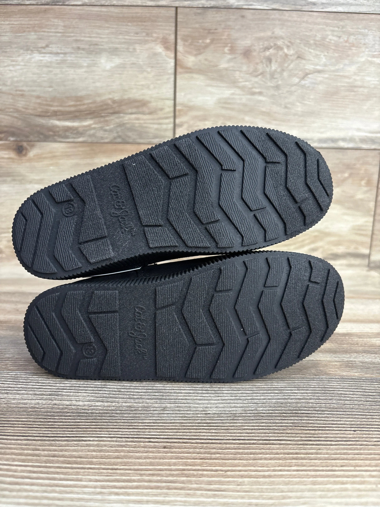 Black rubber soles of children's shoes with textured tread on wood floor