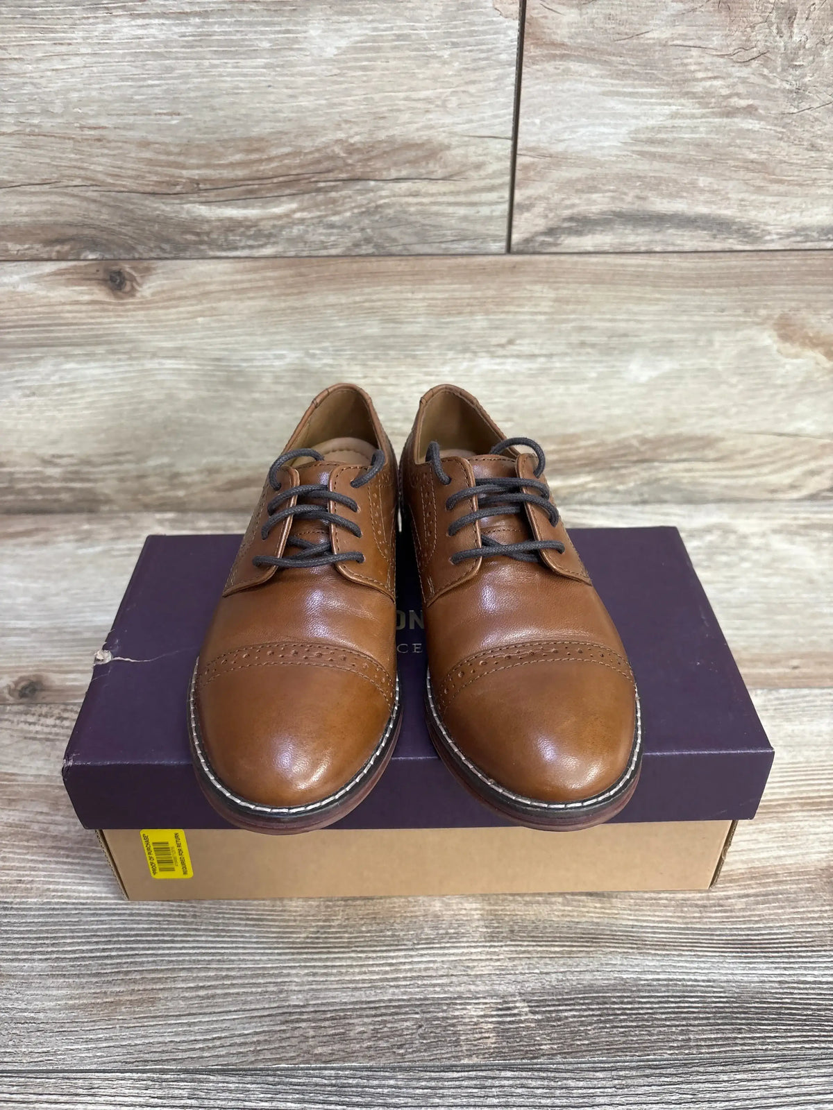 Front view of Johnston and Murphy cap-toe brown leather dress shoes size 12C showing brogue detail and black laces on shoebox