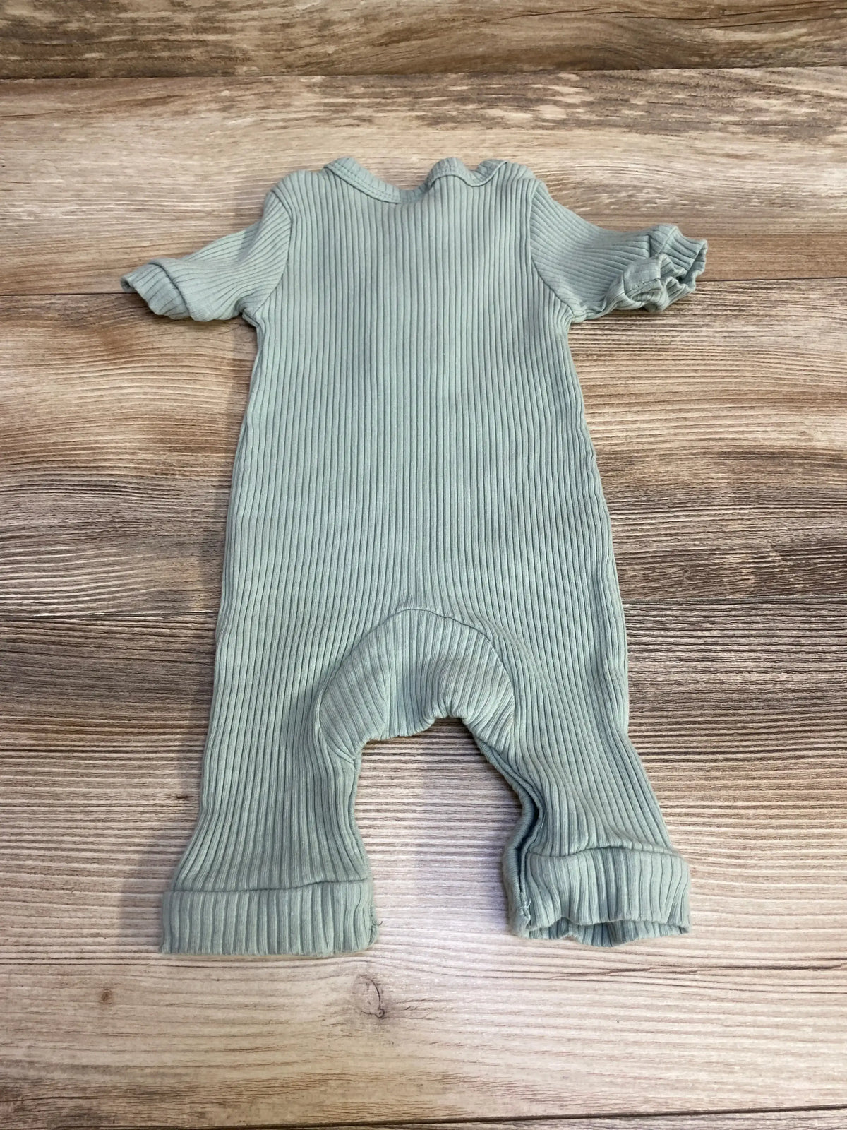 Back view of green ribbed henley romper (3M) with ruffled short sleeves, cuffed legs and vertical ribs on wood background