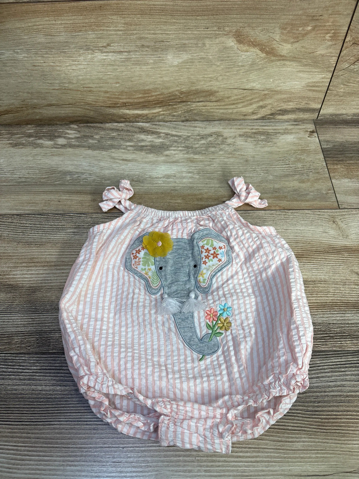 Front view of Goodlad pink striped seersucker romper with embroidered elephant and ruffled leg openings on wood-look floor