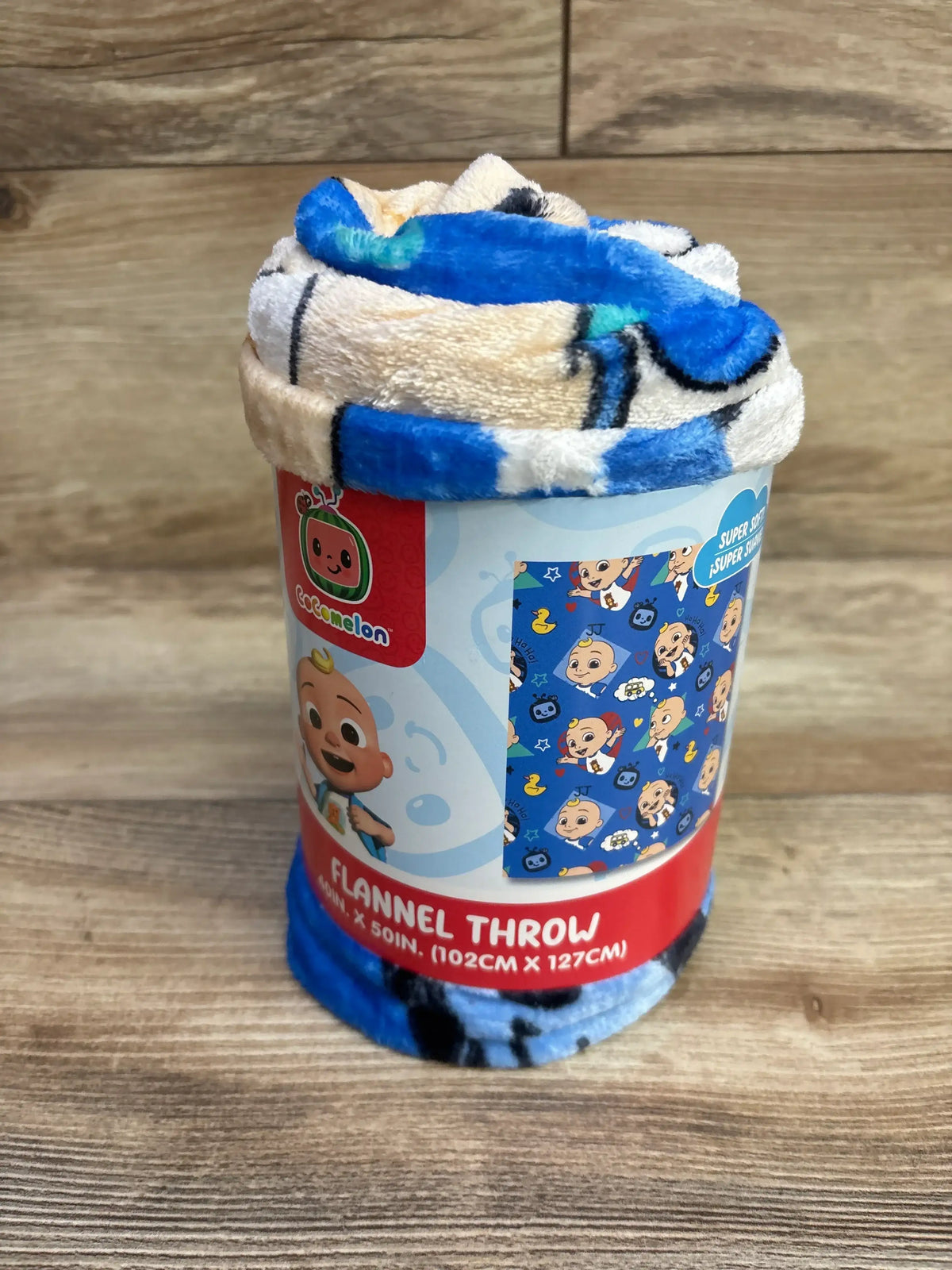 Front view of rolled Cocomelon blue flannel throw showing character print and packaging label with size 40 x 50 in on wood tabletop