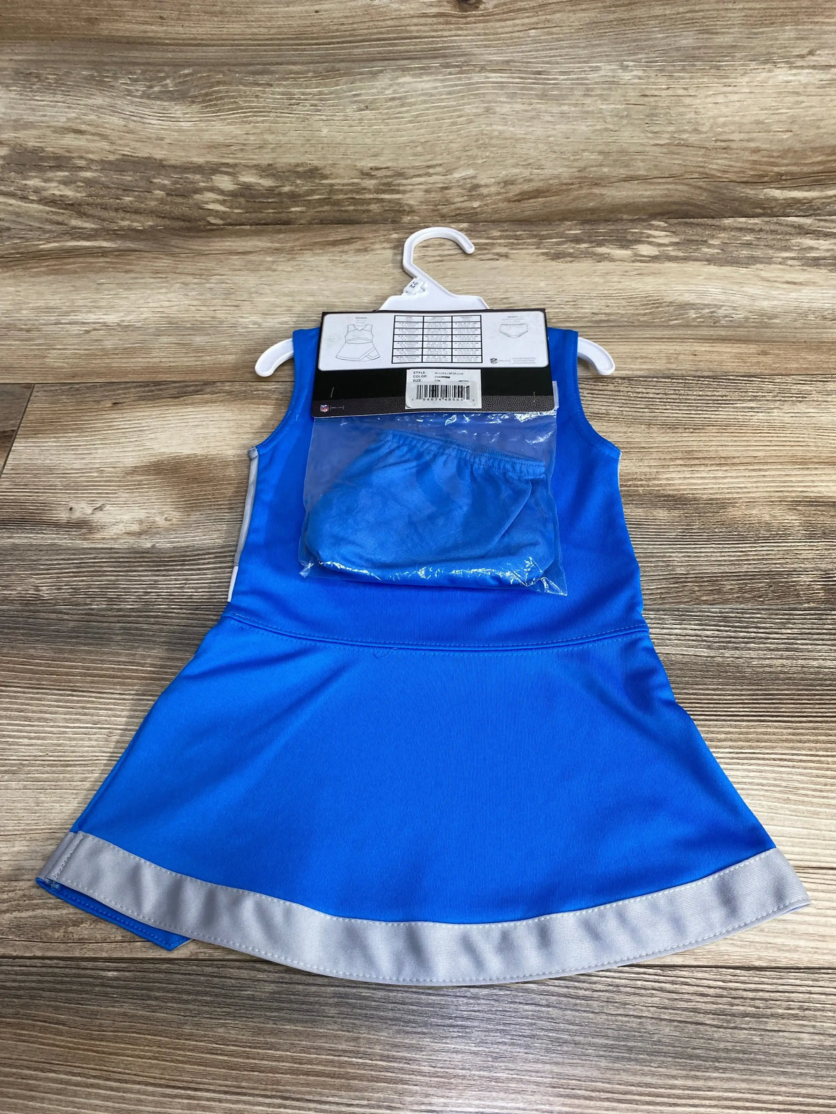 Flat lay of Los Angeles Chargers toddler cheer jumper dress with silver hem and packaged matching bottoms on wood floor