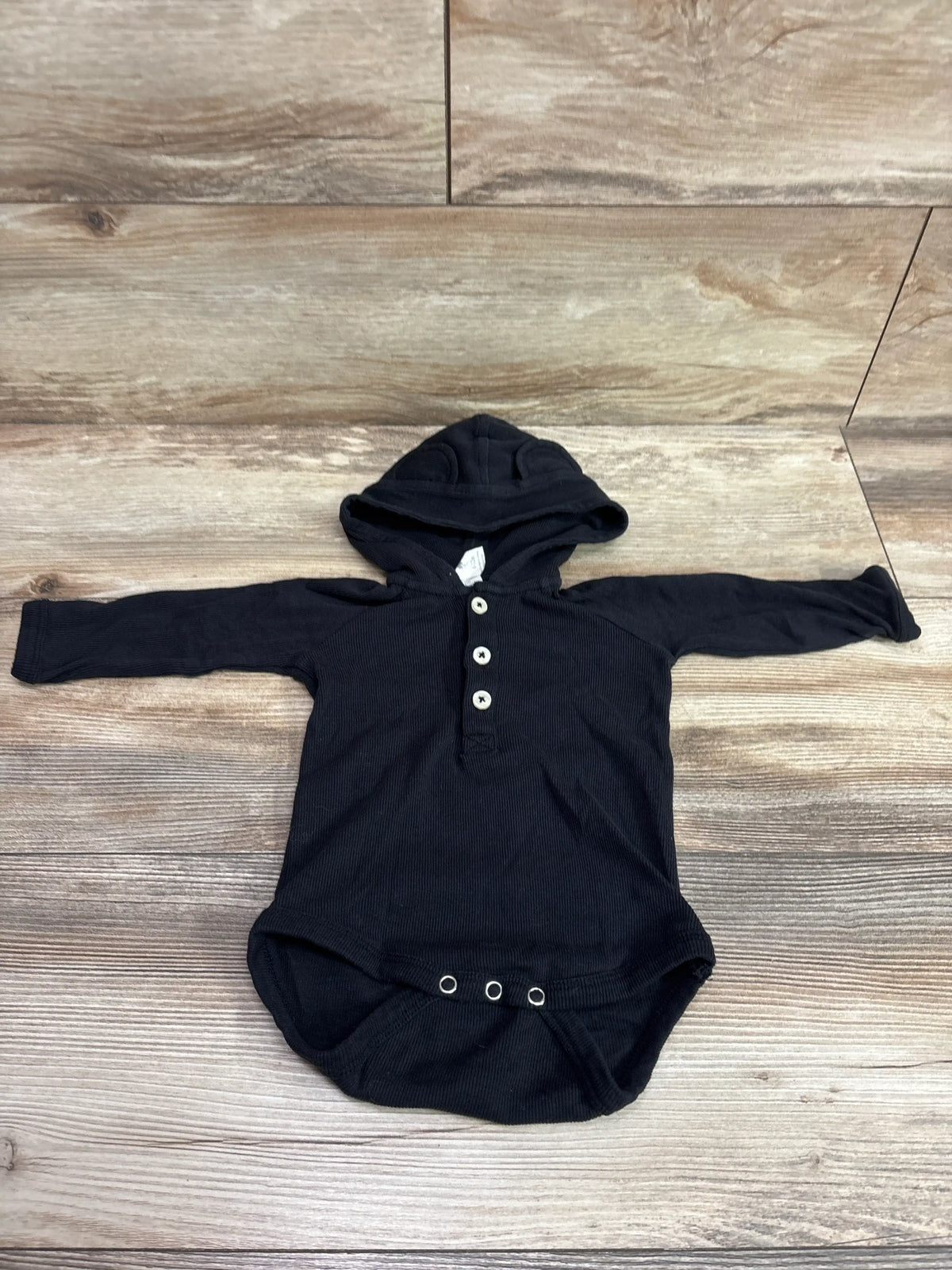 Kate Quinn black ribbed hooded henley bodysuit for babies on a wood background