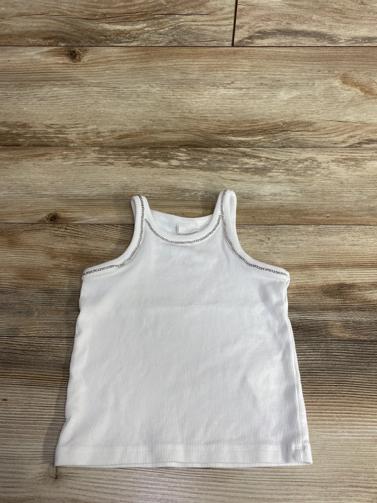 White sleeveless toddler tank top with silver trim on wooden surface, kids clothing resale item