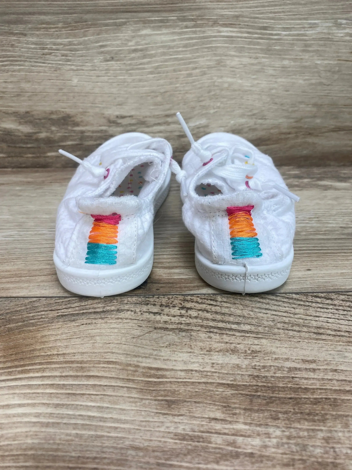 Rear view of white girls' bump-toe sneaker, size 10C, showing multicolor embroidered heel tab on wood background