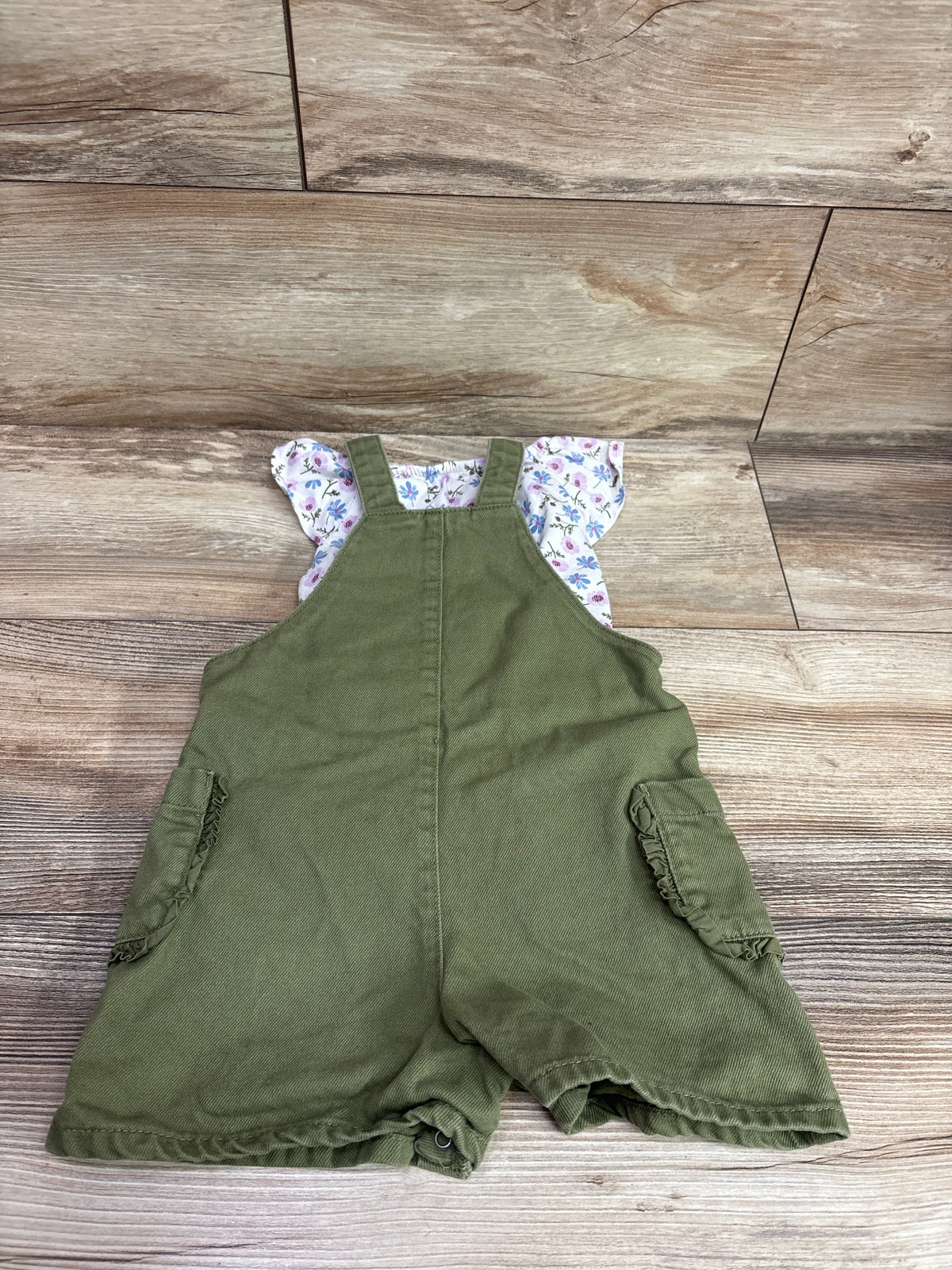 Front view of Obaibi floral shirt and shortalls set showcasing olive green shortalls and floral puff sleeves on a wood floor
