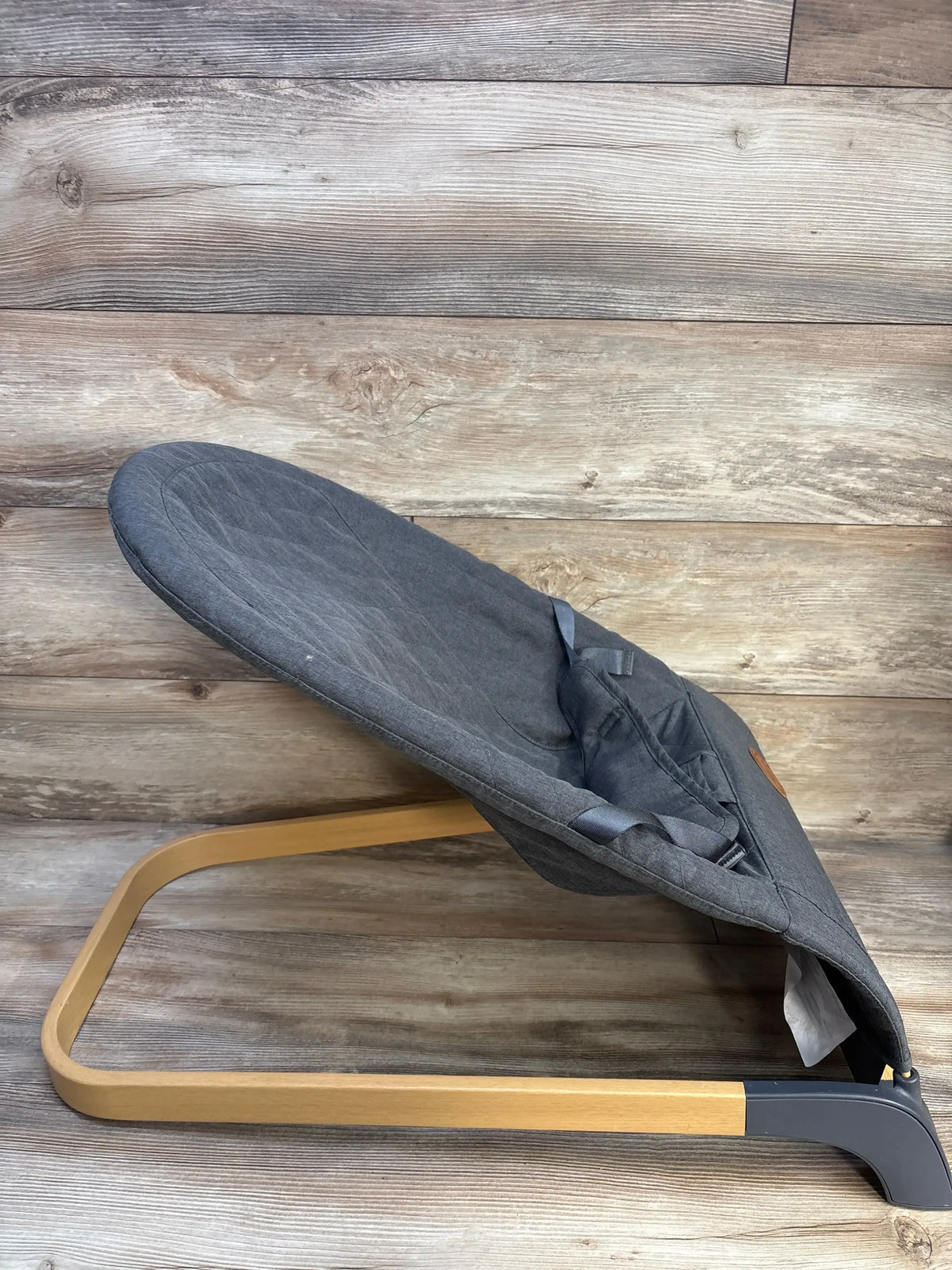 Side view of ANGELBLISS portable baby bouncer in grey showing curved wooden base and fabric seat on wood background