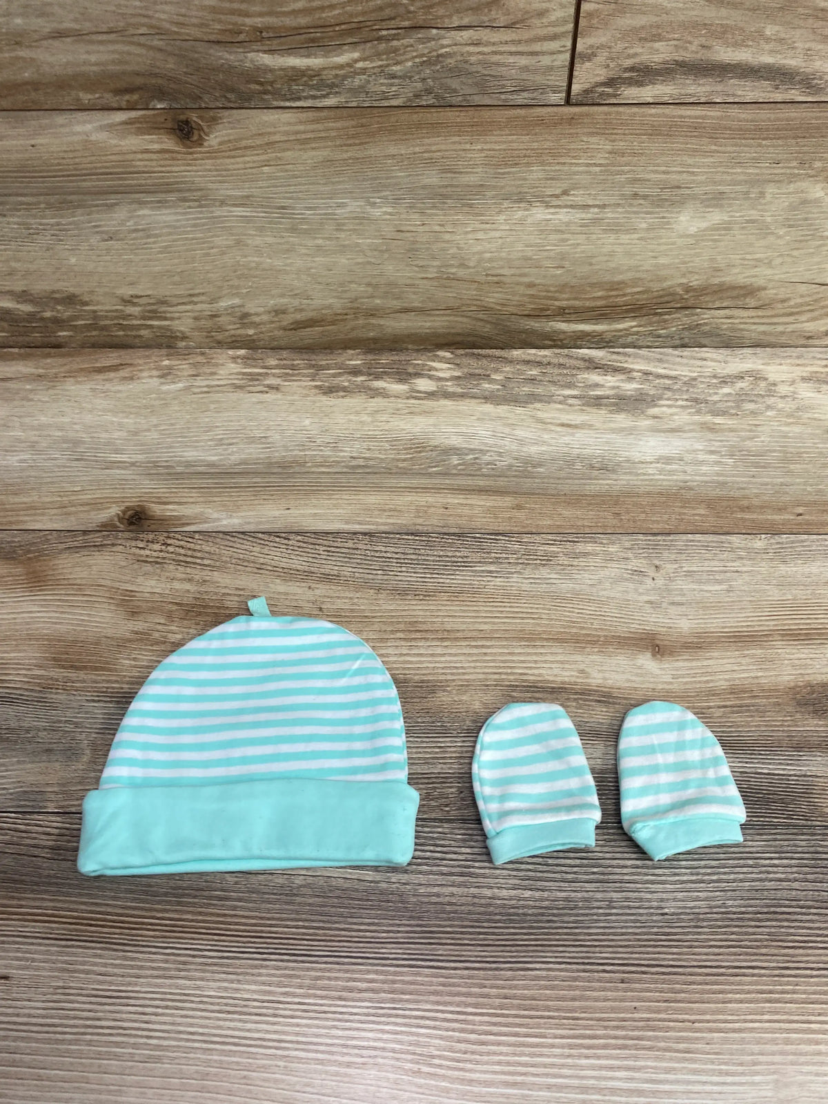 Aqua and white striped 2pc cap and mittens set for baby on a wooden background.