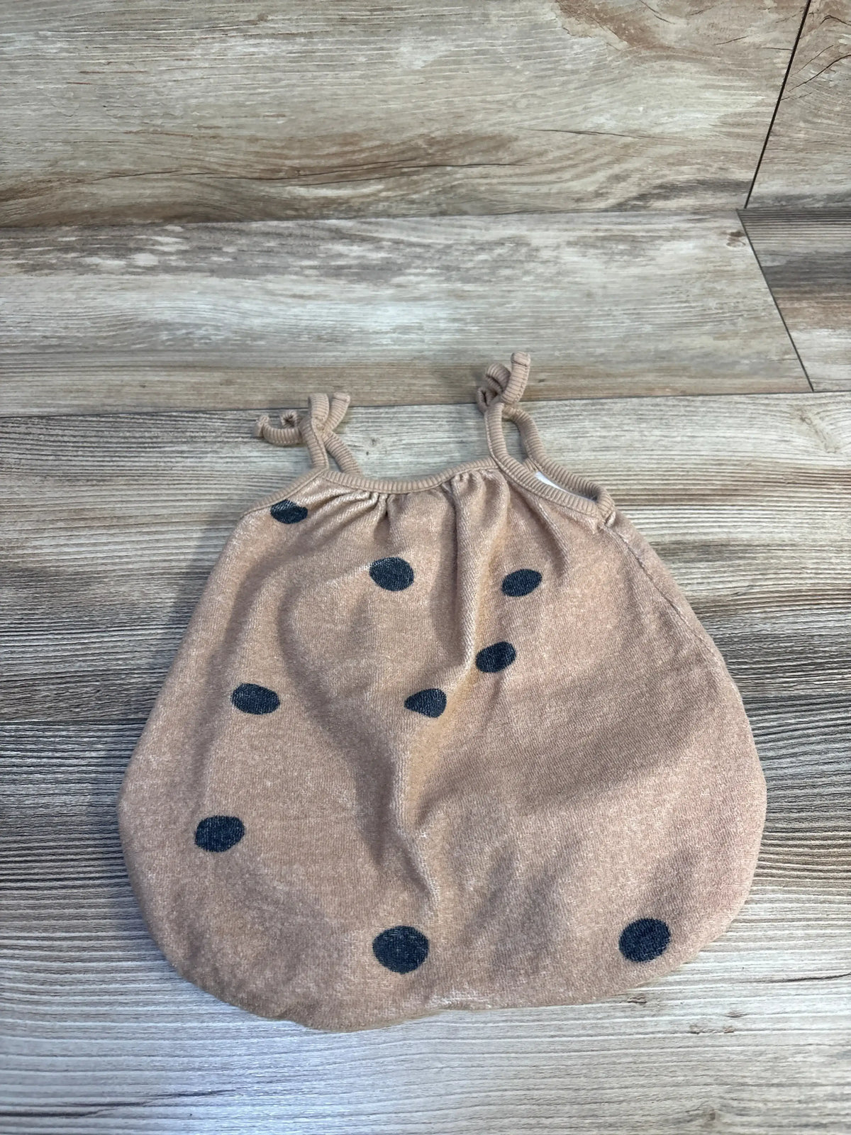 Top-down view of Grayson terry bubble romper tan with navy polka dots and knotted shoulder straps on wood background