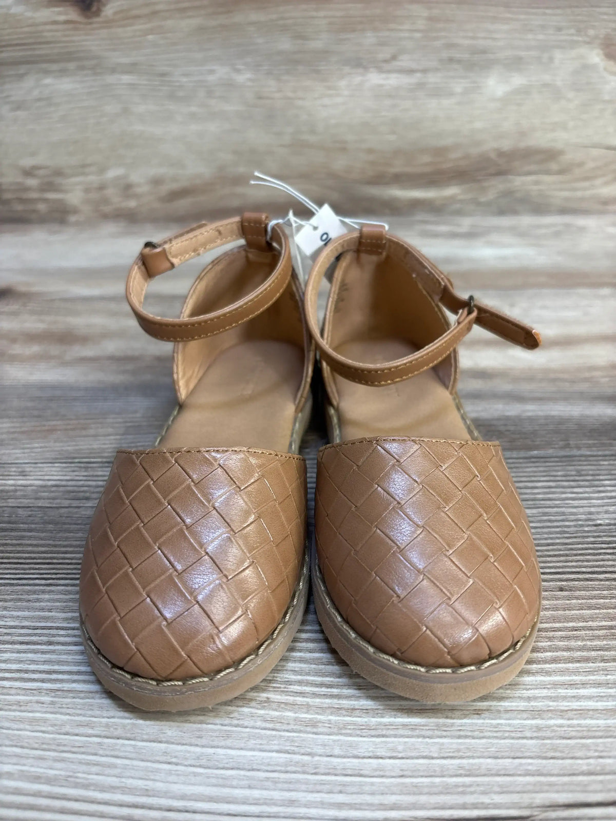Brown woven faux leather girls' closed-toe sandals with ankle straps on wooden background