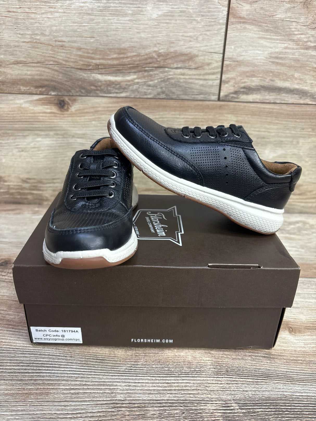 Black kids sneakers with white soles displayed on a shoebox, wooden background