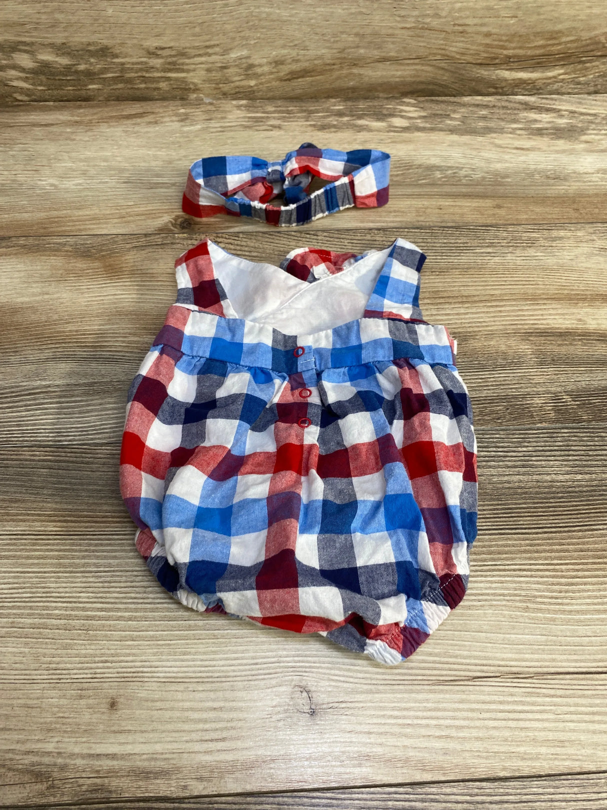 Flat lay of newborn plaid romper with matching headband, showing front buttons and elastic legs on light wood background