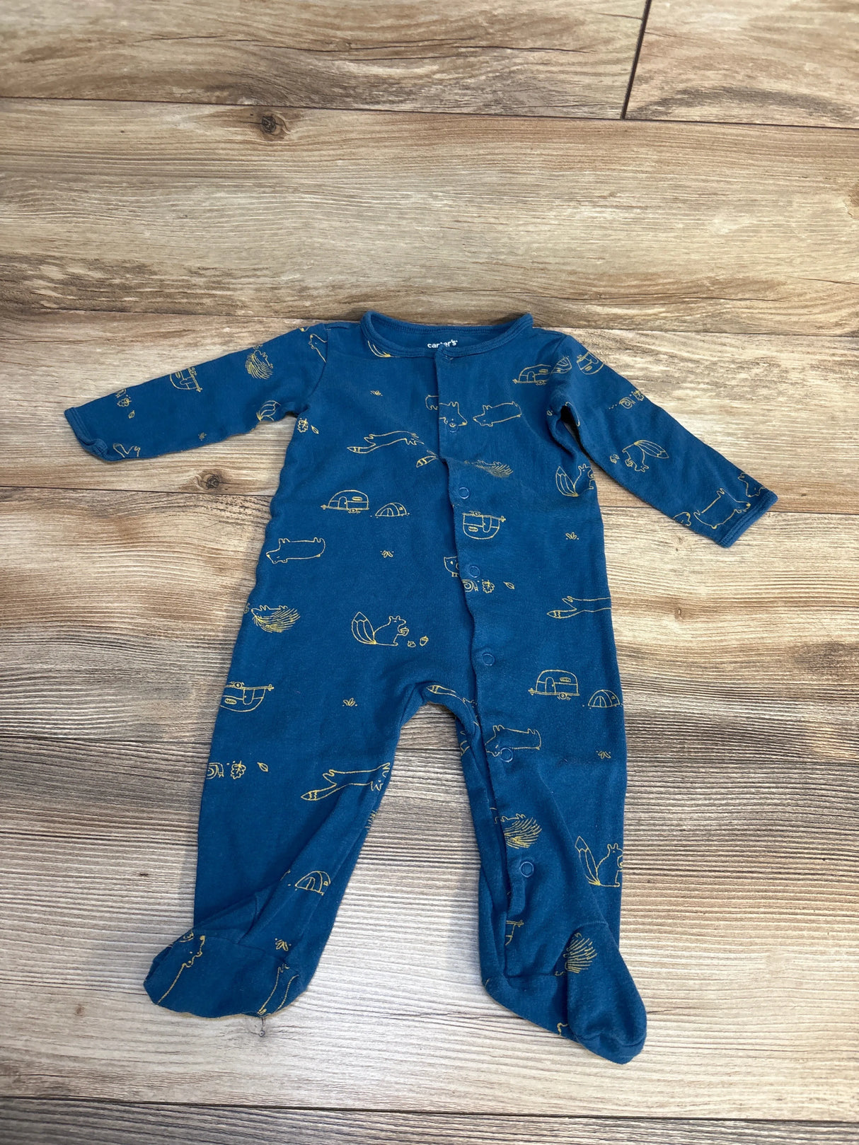 Blue Carter's baby footed pajamas with yellow camping and animal print, laid on wood floor
