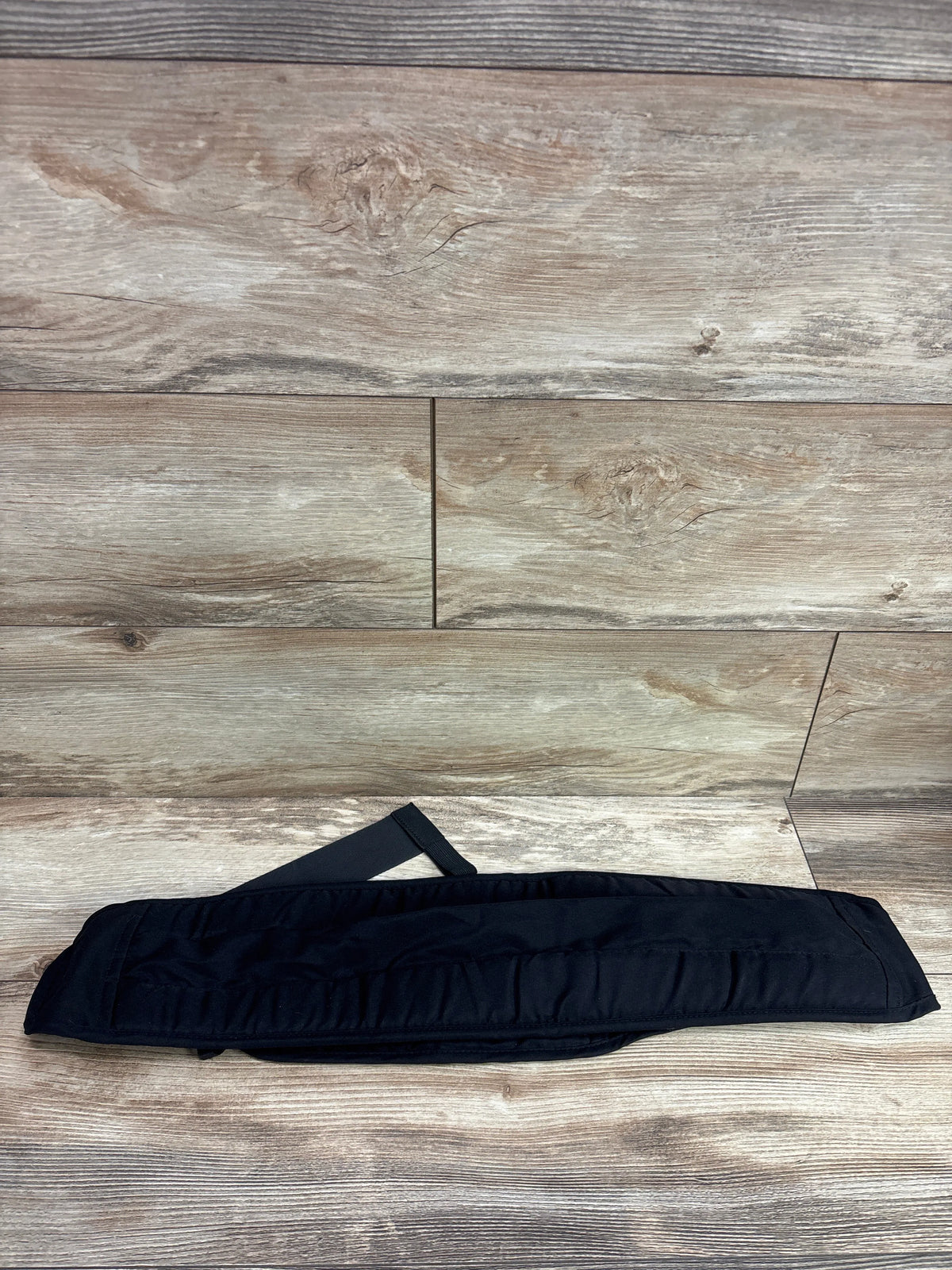 Top view of black Senerah sling carrier showcasing its padded panel and strap on a wood-look floor