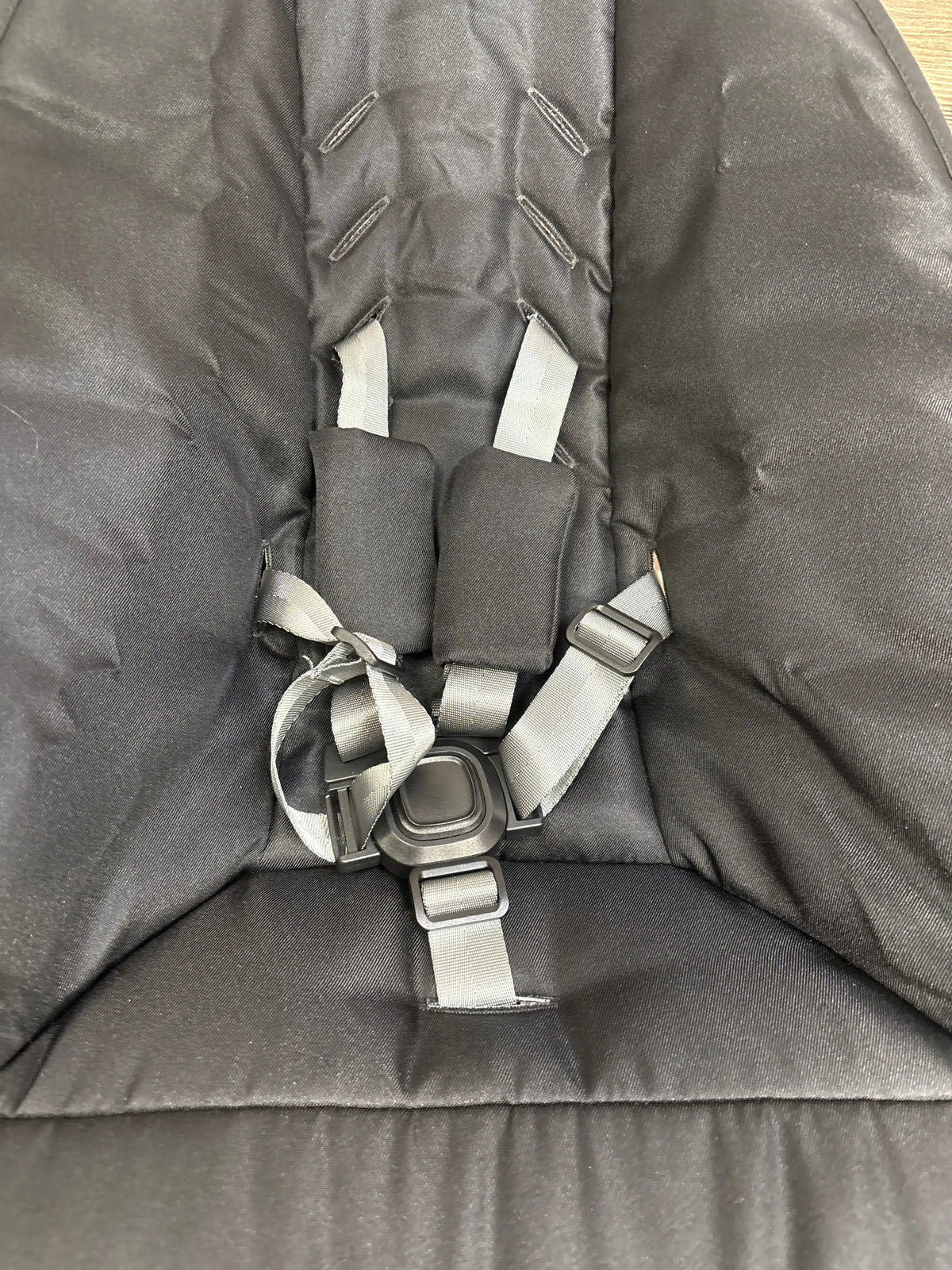 Close-up of 4moms mamaRoo Multi-Motion Baby Swing showcasing its padded five-point harness and buckle on a black seat