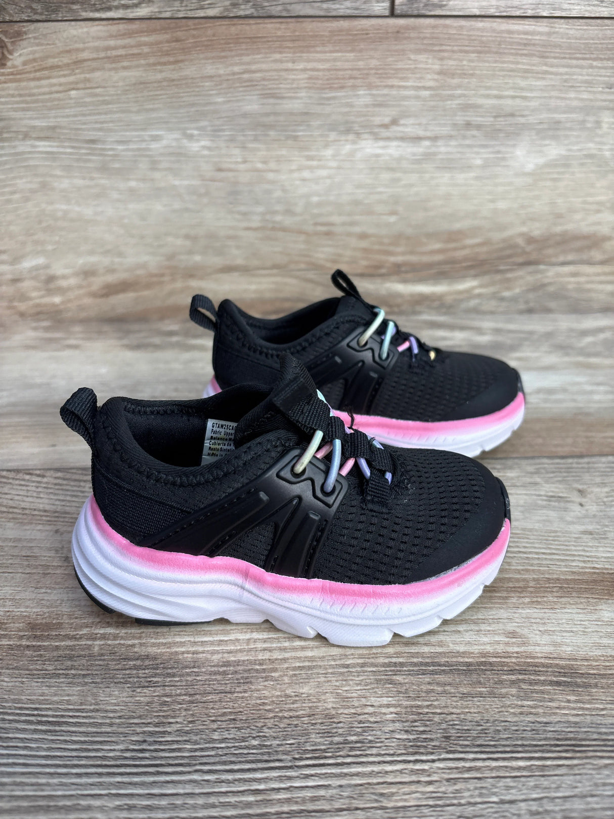 Kids black athletic sneakers with white soles and pink trim on wooden surface