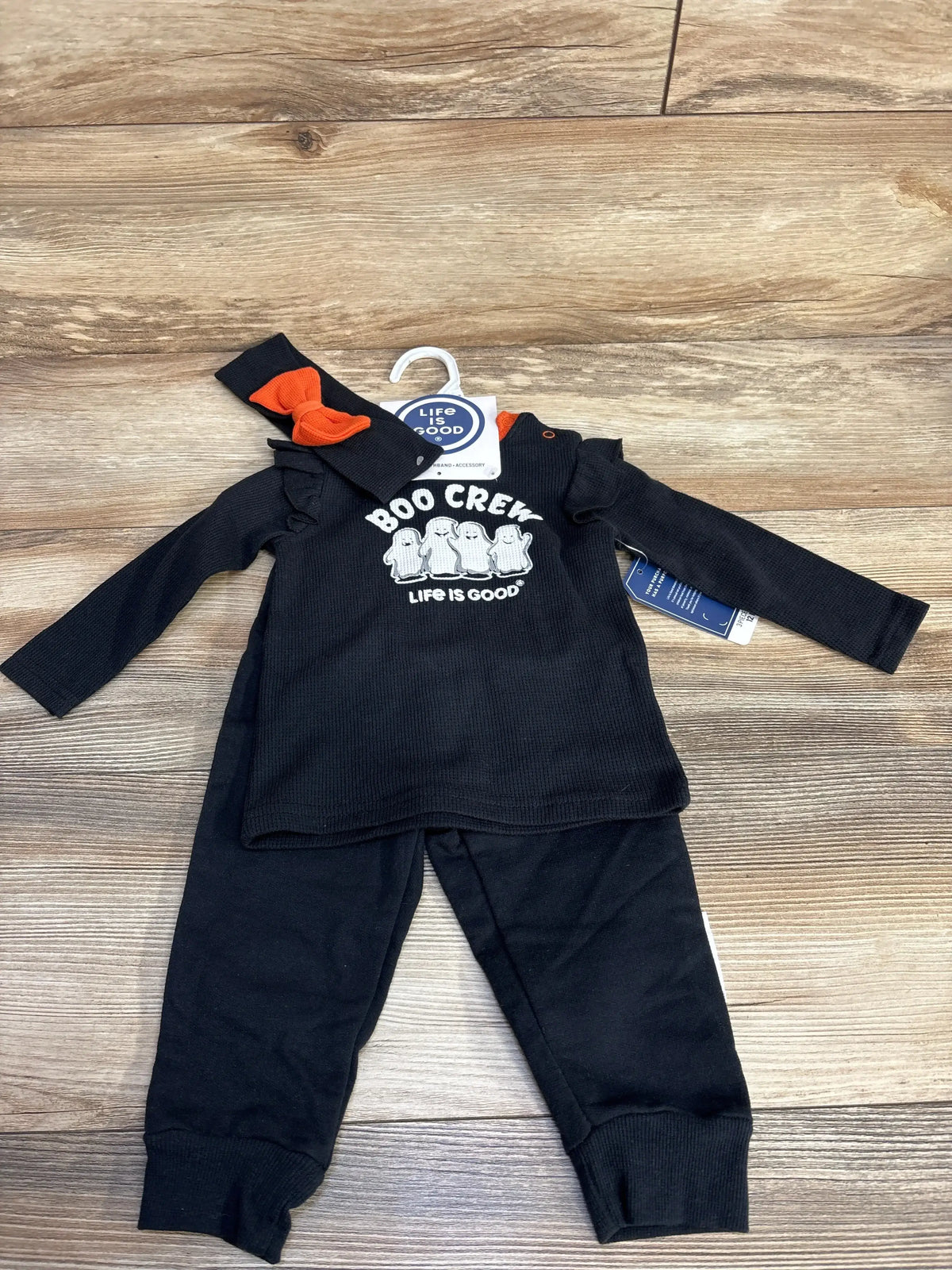 Front view of black Life Is Good Boo Crew 3 piece baby set with long sleeve top, pants, and orange bow headband, size 12 months