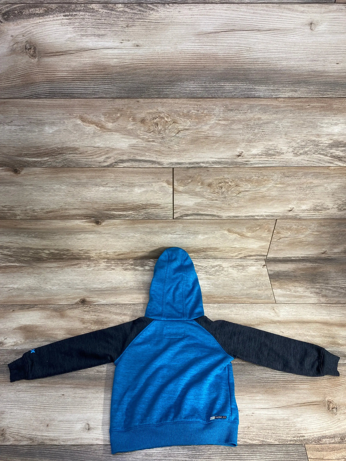 Back view of toddler Hurley pull-over hoodie (2T) in blue with black sleeves, hood, and Therma-FIT tag on wooden floor