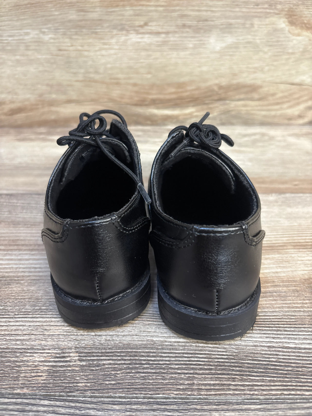 Rear view of black kids' dress shoes with laces on wood background