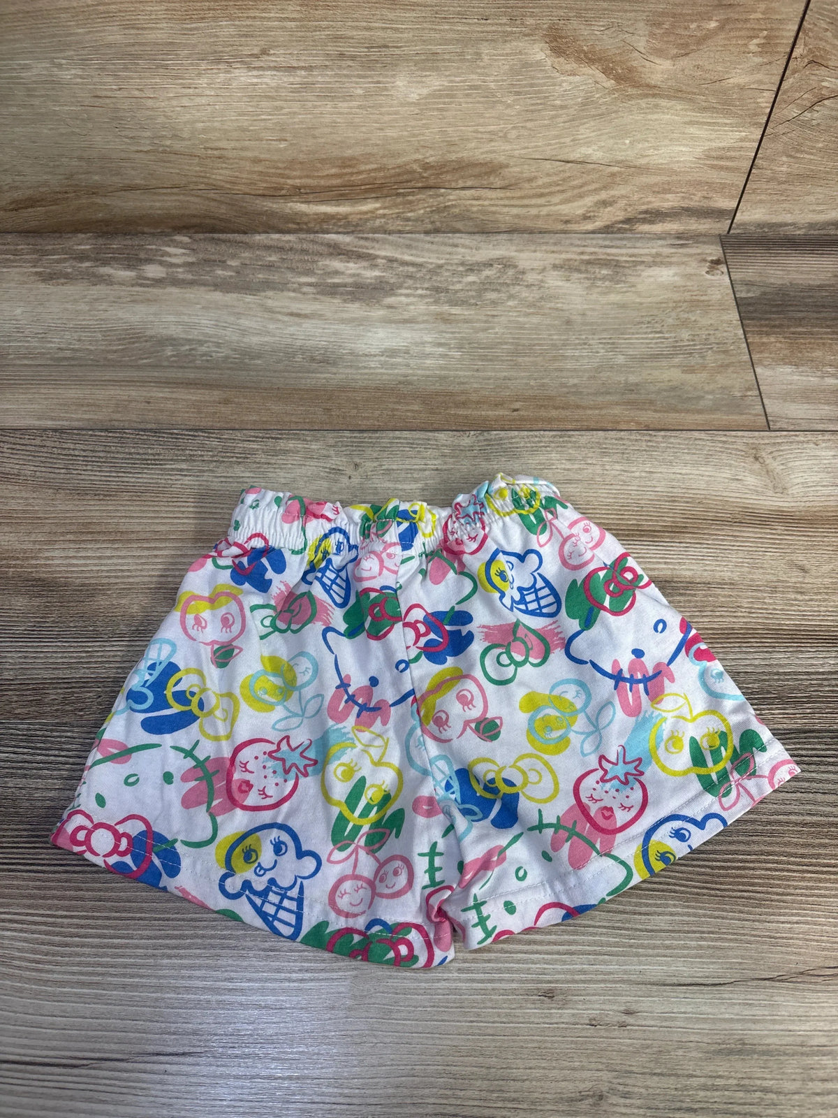 Top view of Hello Kitty shorts in white, size 4T showcasing colorful character print and elastic waistband on a wood floor