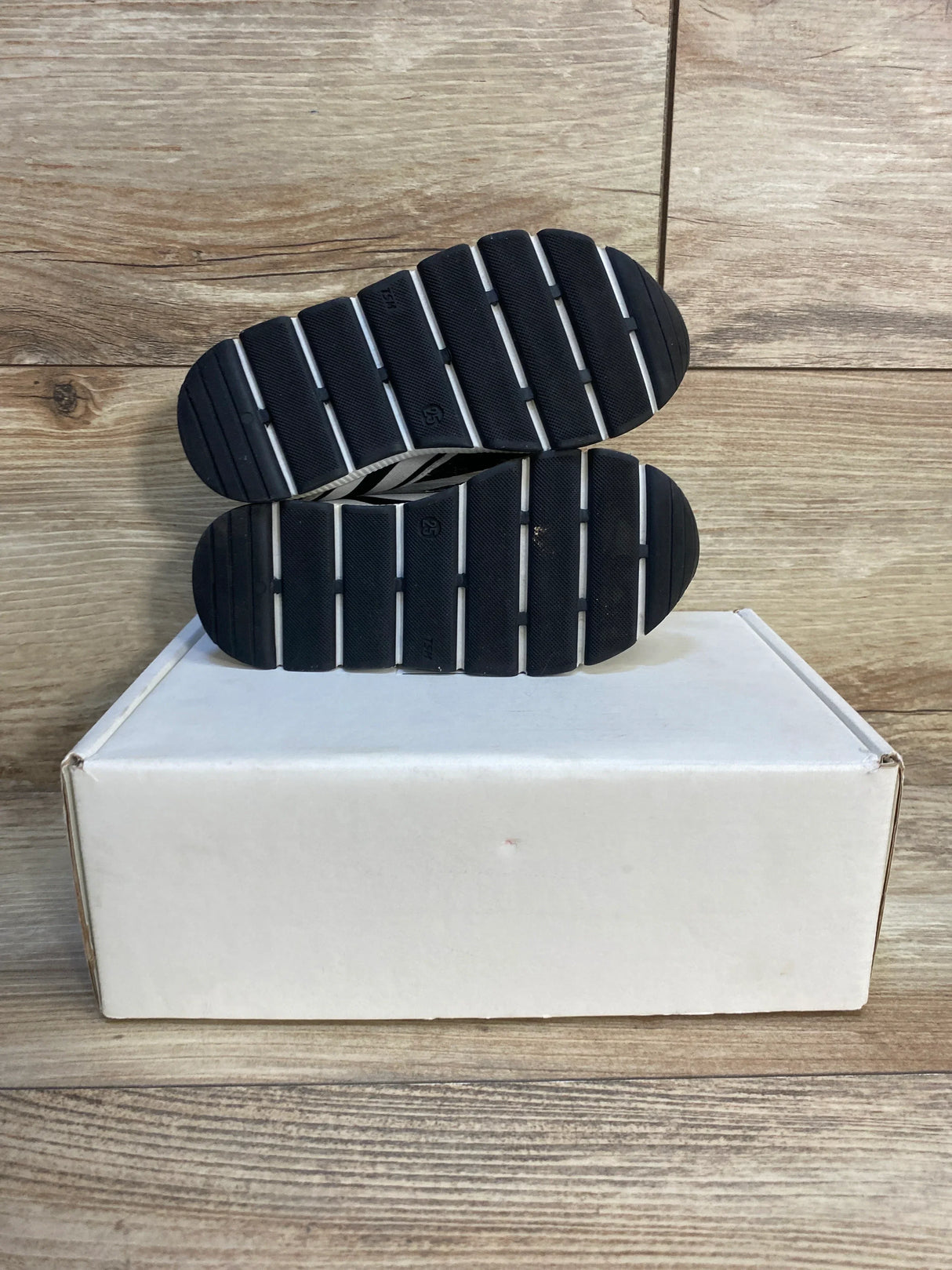 Black-soled toddler shoes on a white box with wood background, kids footwear resale