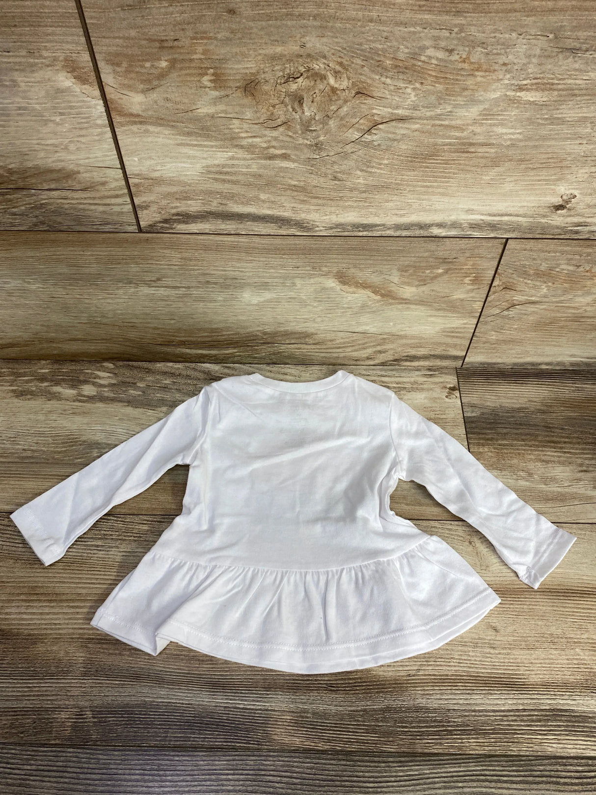 White long-sleeve baby shirt with peplum hem on wooden floor background