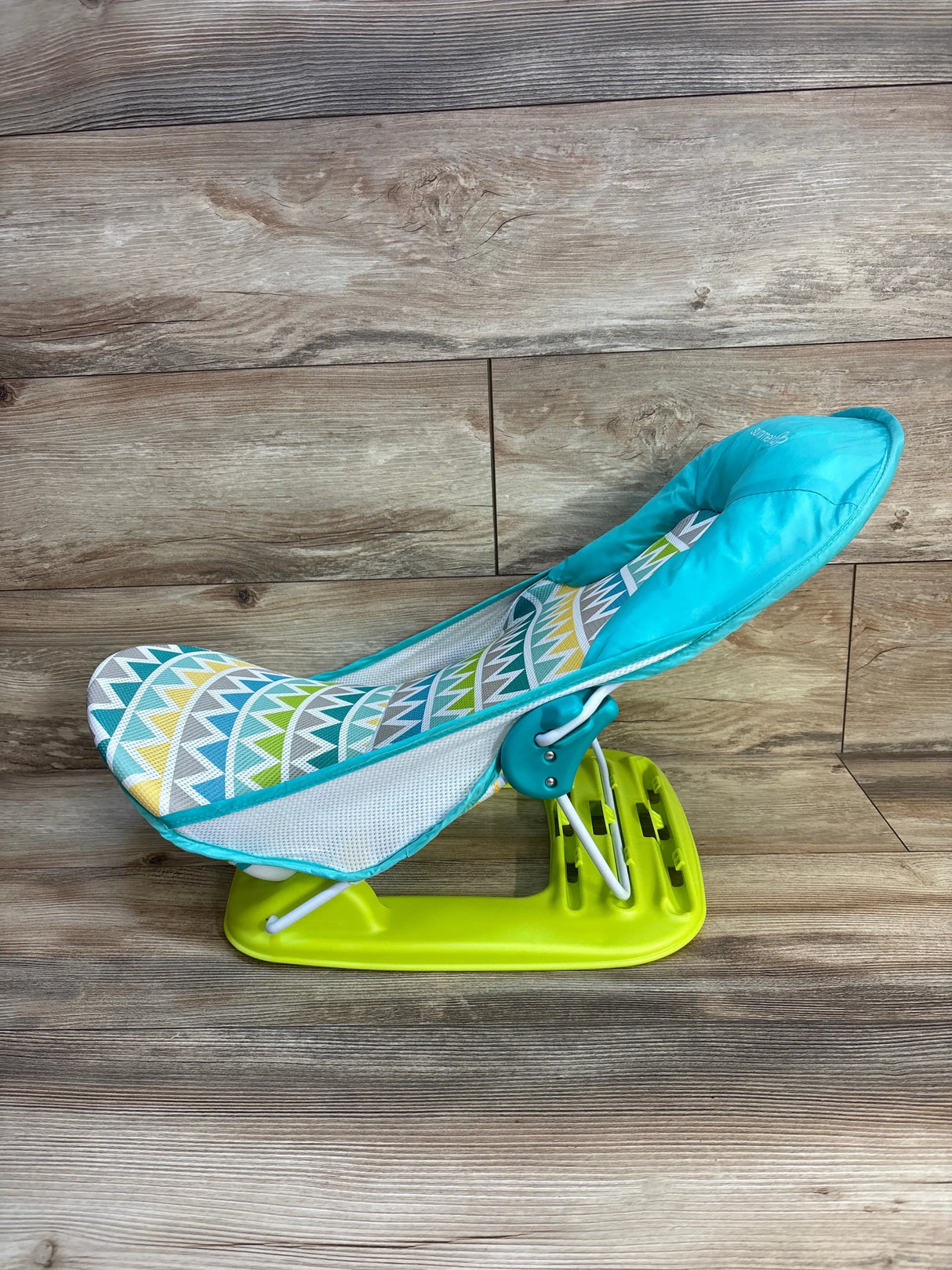 Colorful baby bouncer seat with geometric pattern, turquoise and yellow, on wood floor