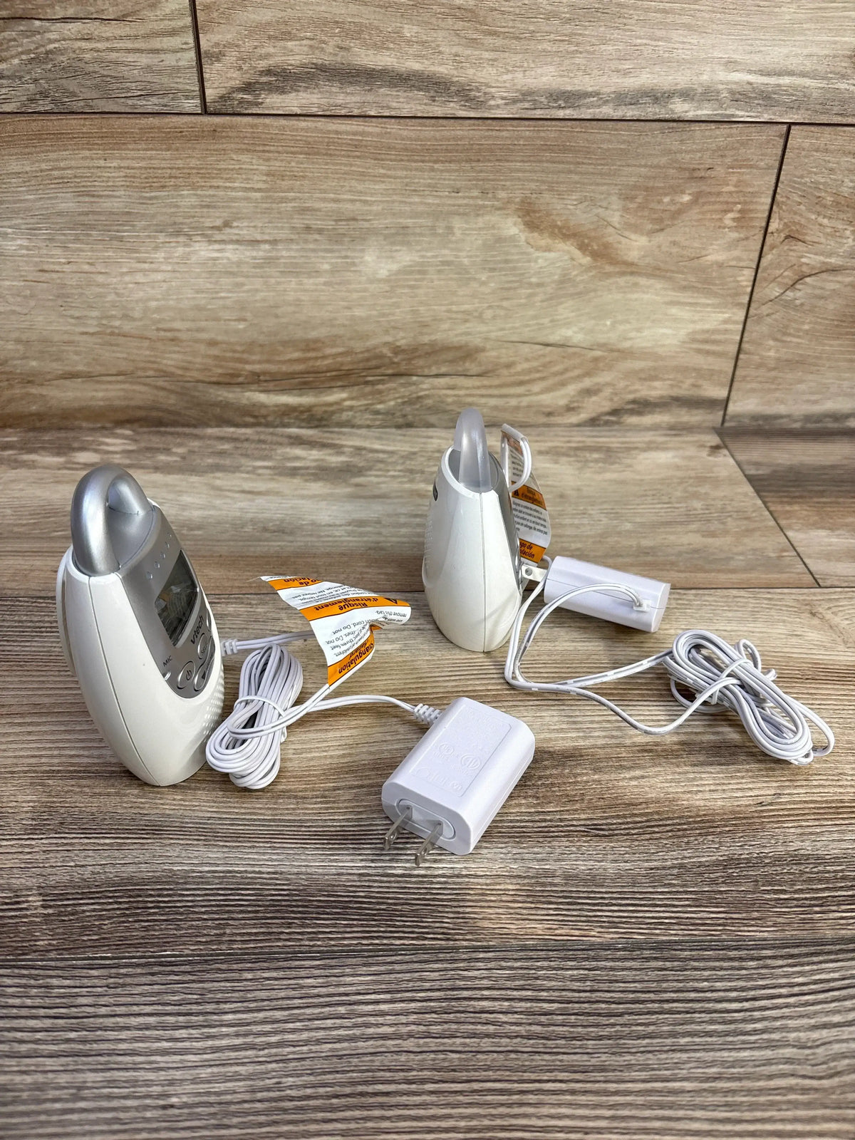 Front and side view of VTech DM221 audio baby monitor showing parent unit display, baby unit, adapter, and cords on wood background