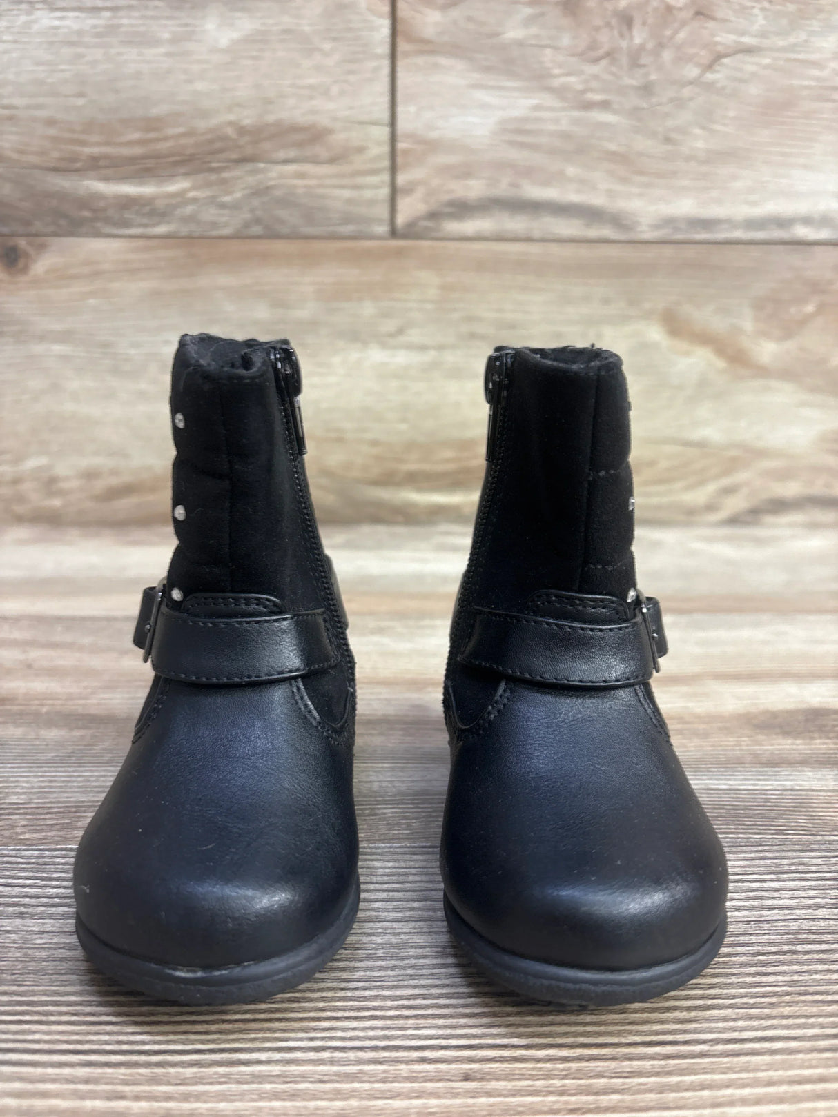 Pair of black toddler boots with side zippers and decorative straps on wood surface