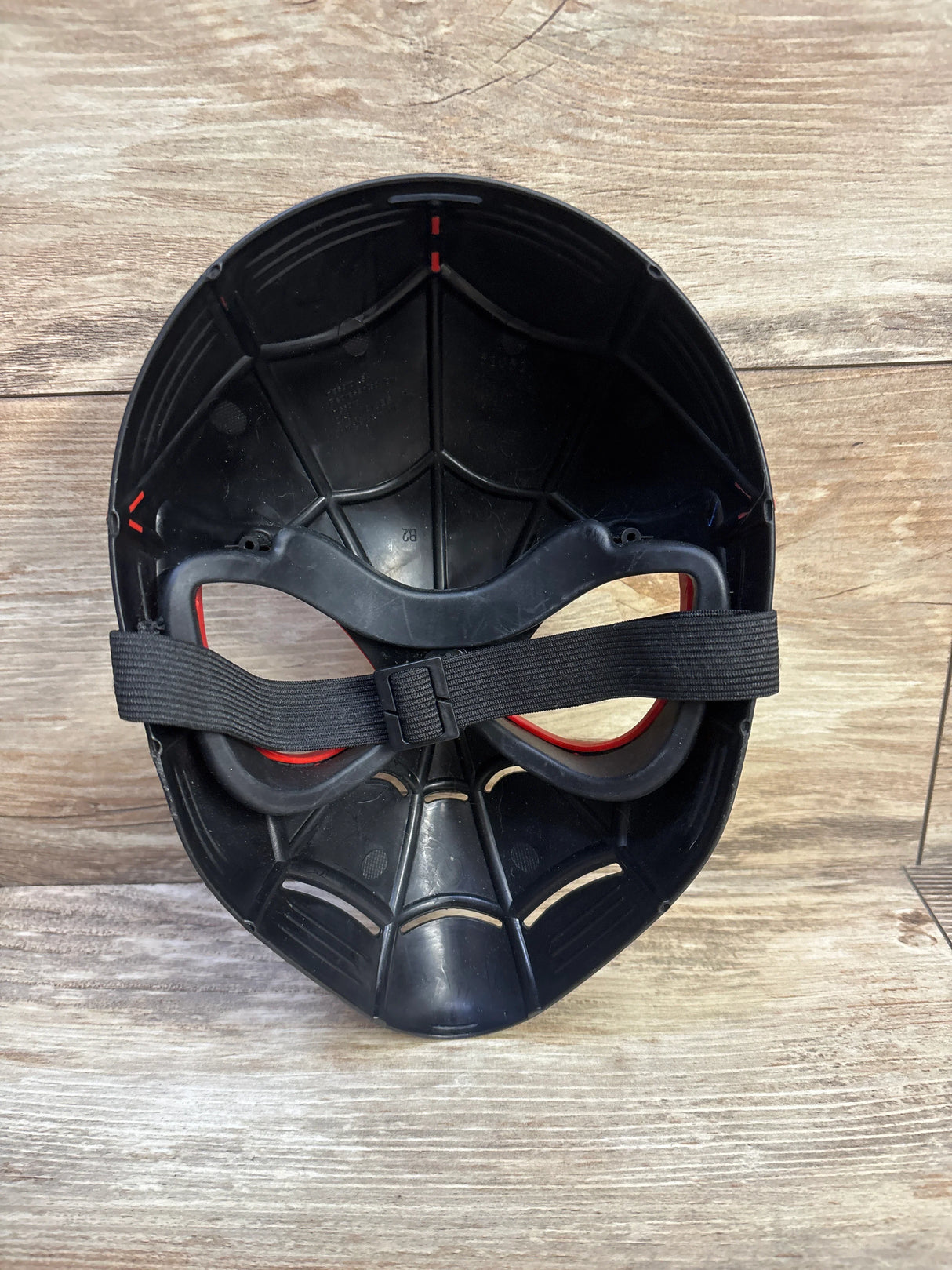Inside view of Spider-Man Miles Morales mask showcasing elastic adjustable strap and molded web interior on wood background