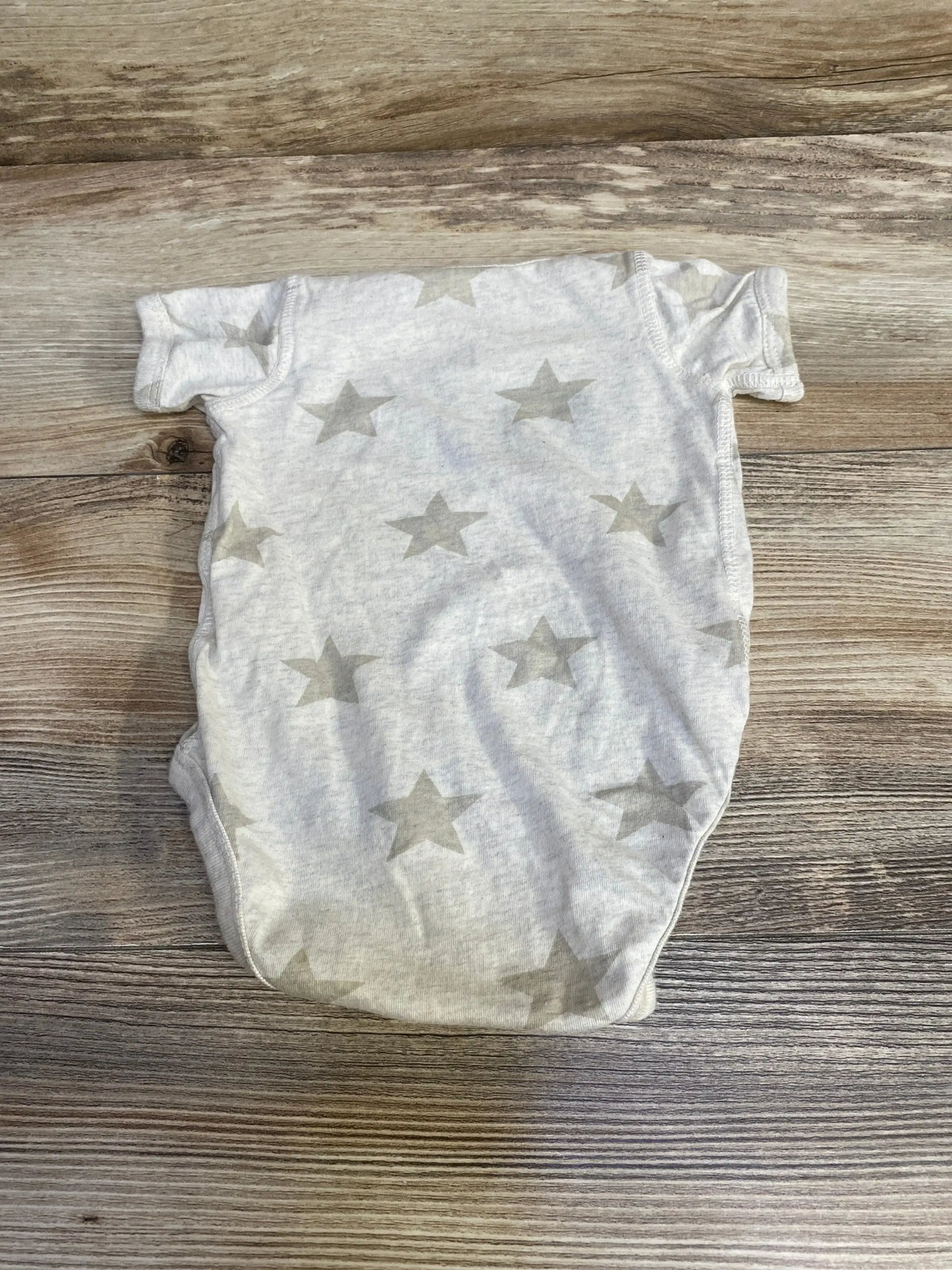 Flat lay of oatmeal 3-6 month baby bodysuit showing gray star print, short sleeves, and snap closure on wood plank background