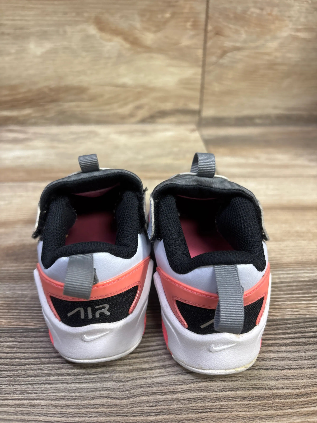 Rear view of Nike Air Max Bolt TD Smoke Grey Pink sneakers showing gray heel pull tabs and pink accents on wood flooring