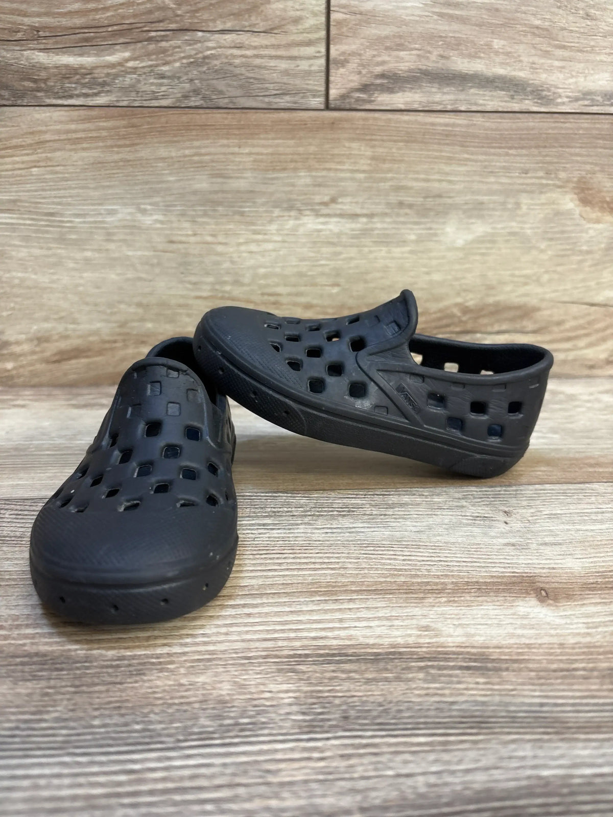 Front three-quarter view of Vans Slip-On TRK toddler sandals 8C black with square cutouts on wood background
