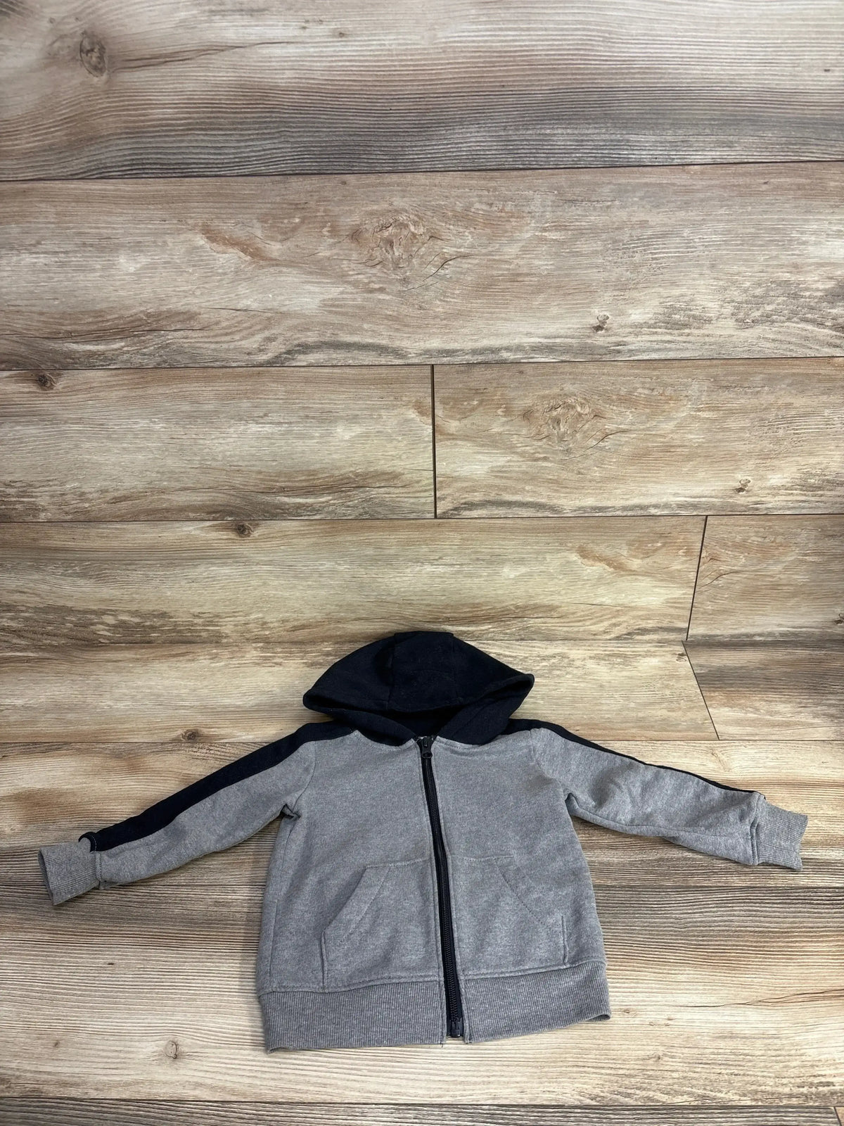 Gray and black kids zip-up hoodie with front pockets laid flat on wood background