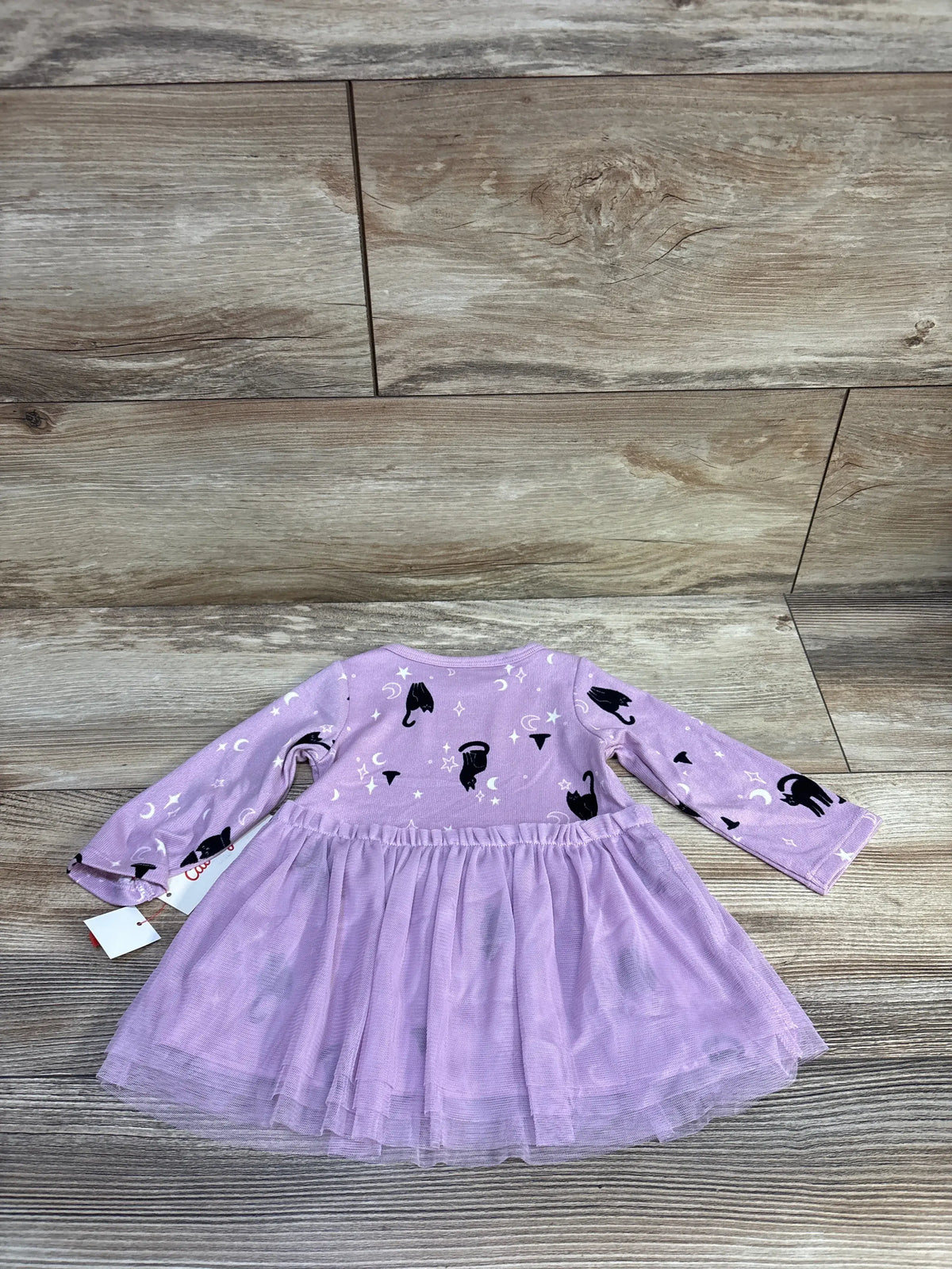 Flat lay of purple long sleeve baby tulle dress with black cat and moon witch print and layered skirt on wood floor