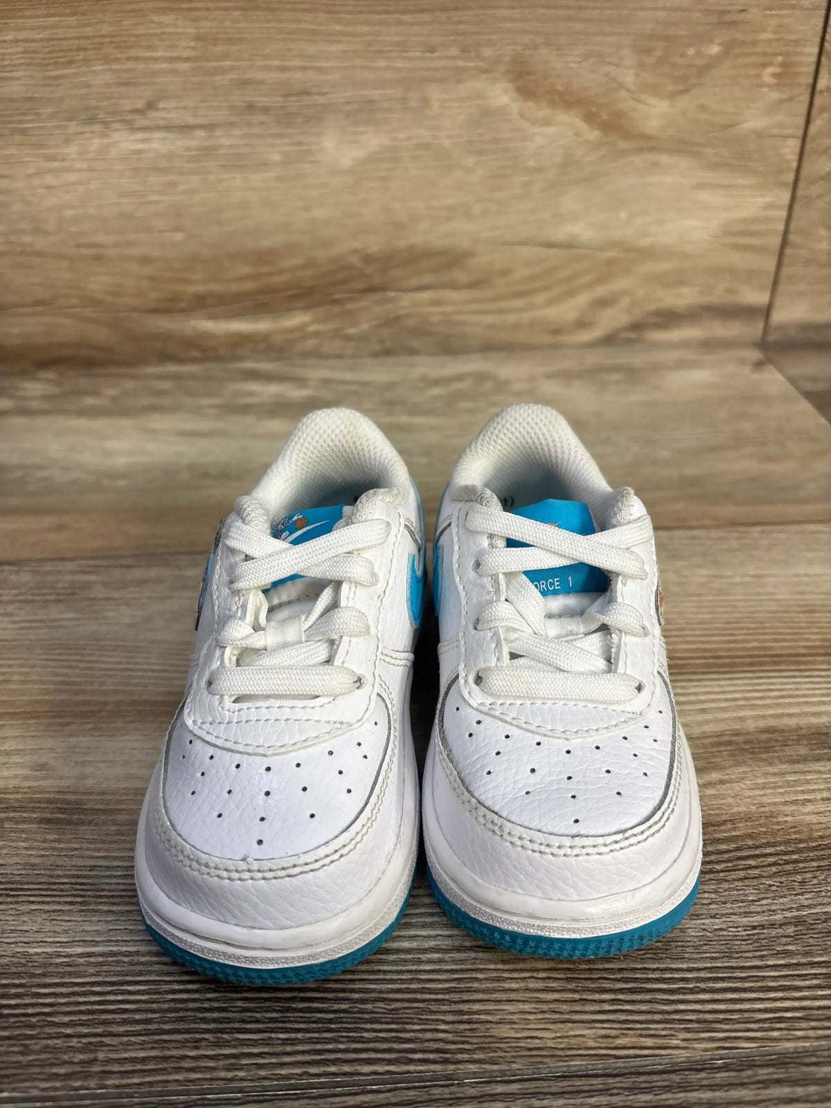 Front view of Nike Air Force 1 TD Space Jam Hare sneakers with white leather uppers and Light Blue Fury overlays on wood floor